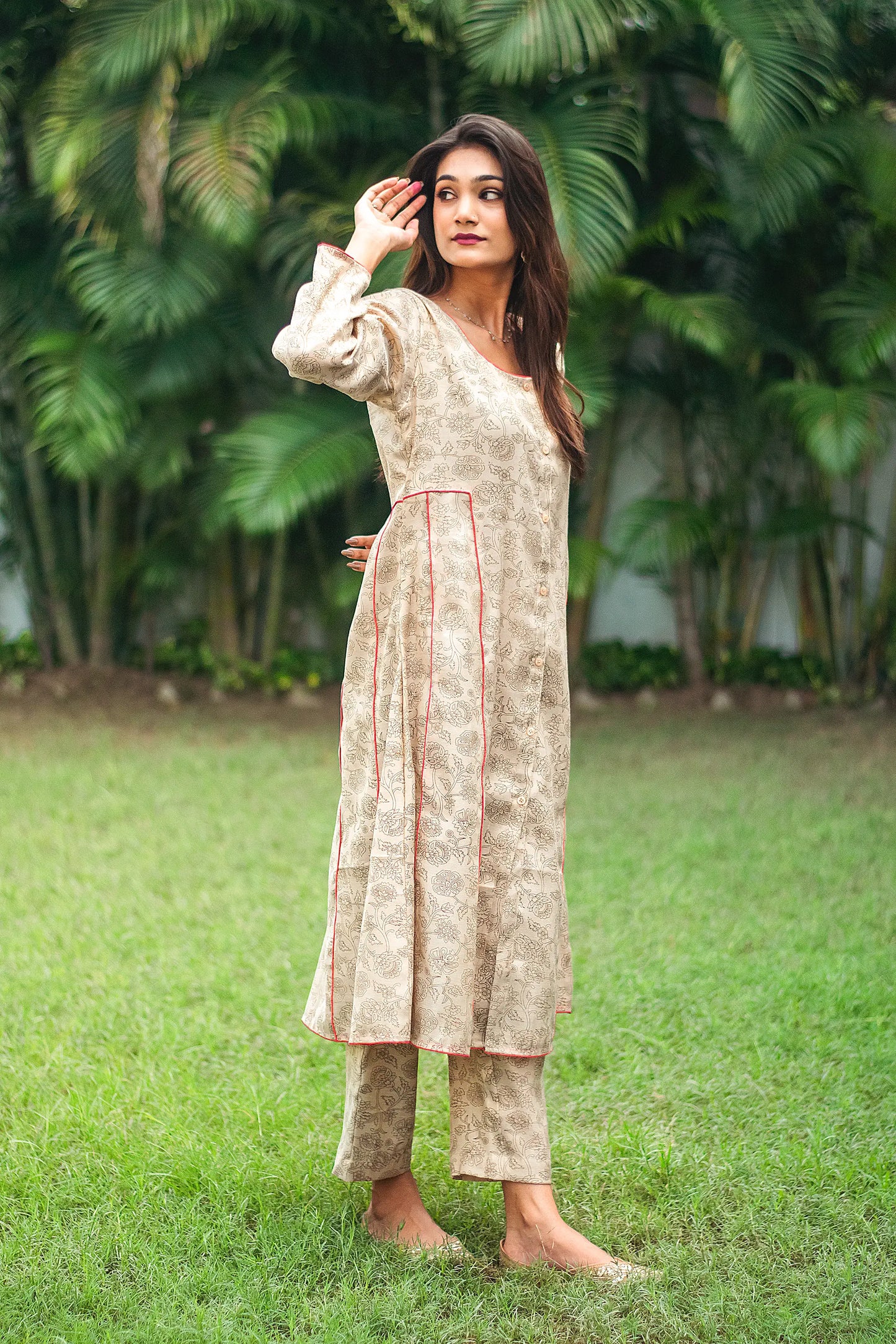 An indian woman wearing a printed staple tussar gold A line kurta and trousers.An indian woman wearing a printed staple tussar gold A line kurta and trousers with gold chanderi dupatta. The A line kurta has double kali in red colour. The woman show case the entire ensemble from her right.