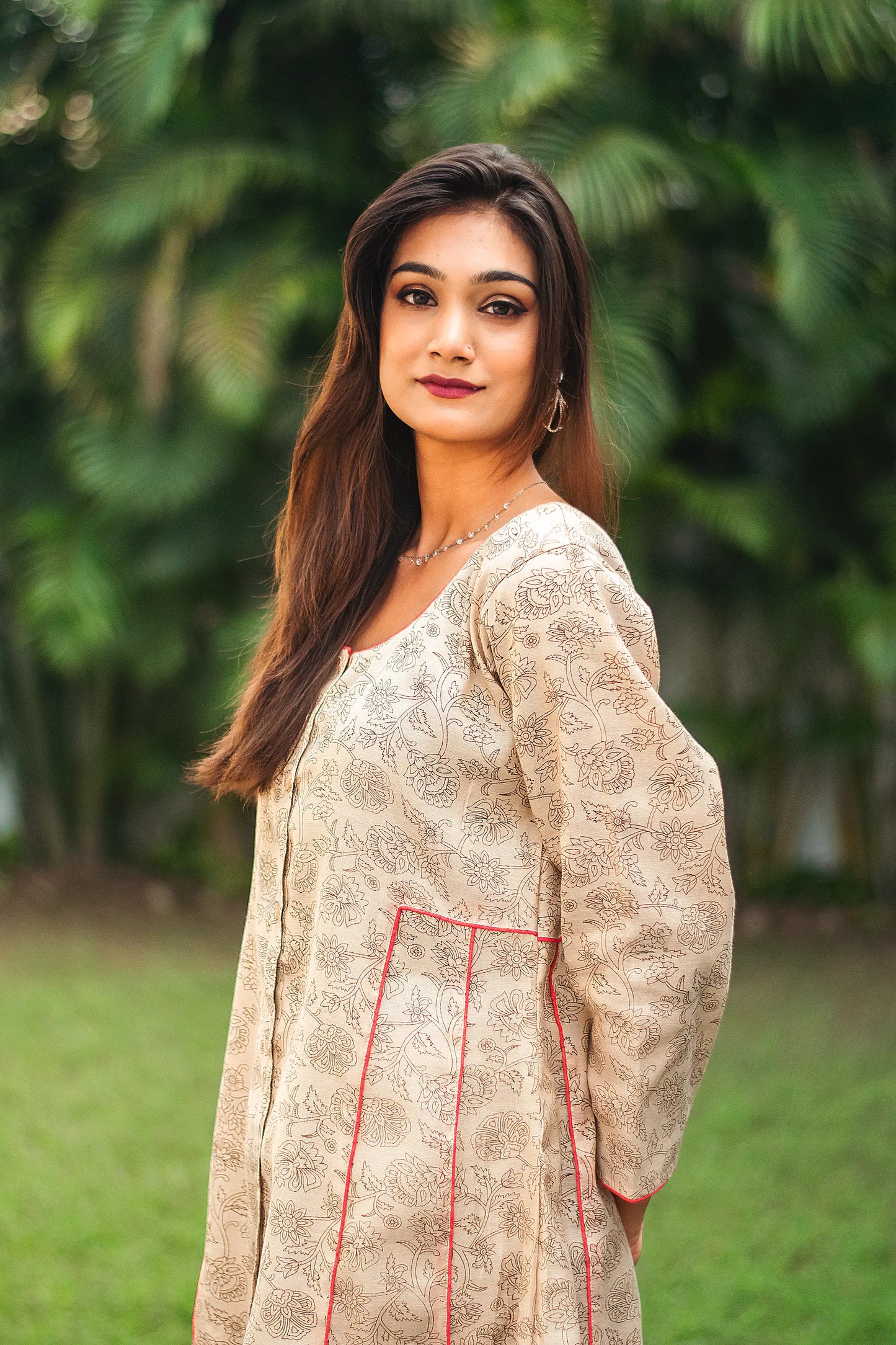 An indian woman wearing a printed staple tussar gold A line kurta and trousers. The A line kurta has double kali in red colour. The woman's left side is facing the camera and the attire is visible from neck till the torso.
