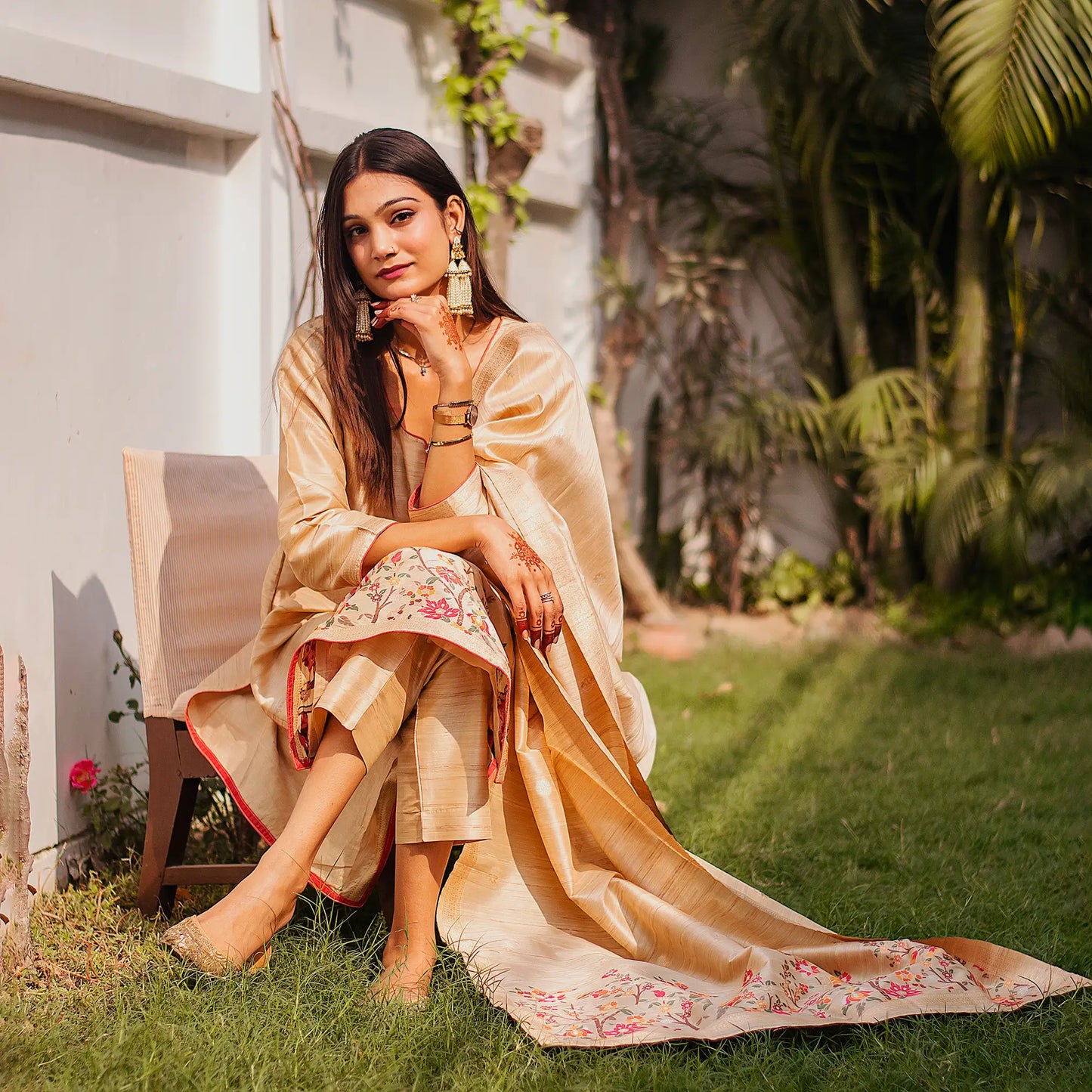 Indian lady poses in a beige silk kurta set with colorful resham vines, paired with a matching dupatta and trousers.