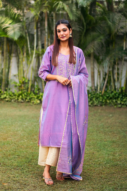 Front view (full suit, top to bottom): Model wearing an iris purple chanderi kurta with beige floral applique work, beige palazzo, and a matching dupatta.