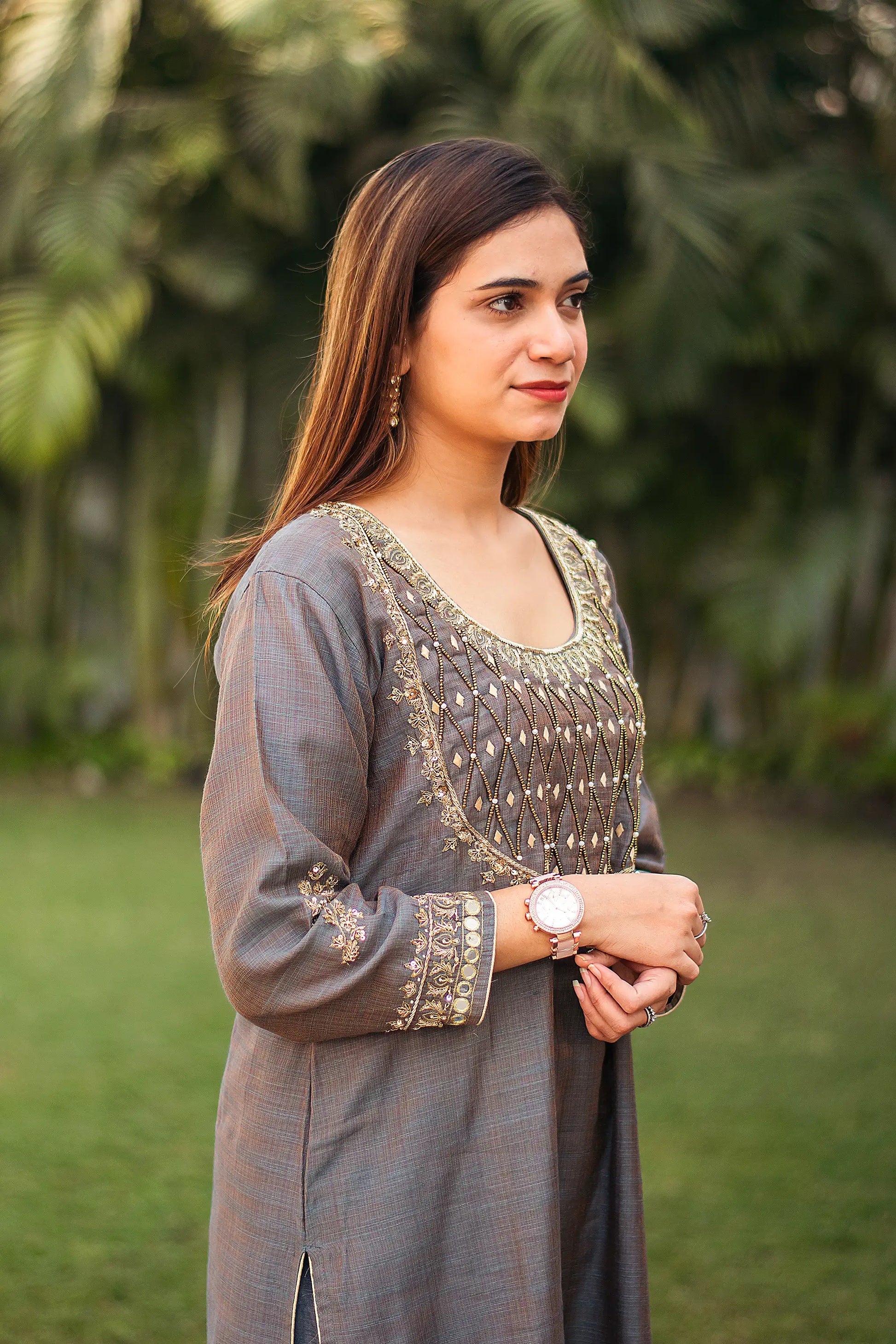 Indian model  poses sideways wearing a silk kurta with golden embroidery.