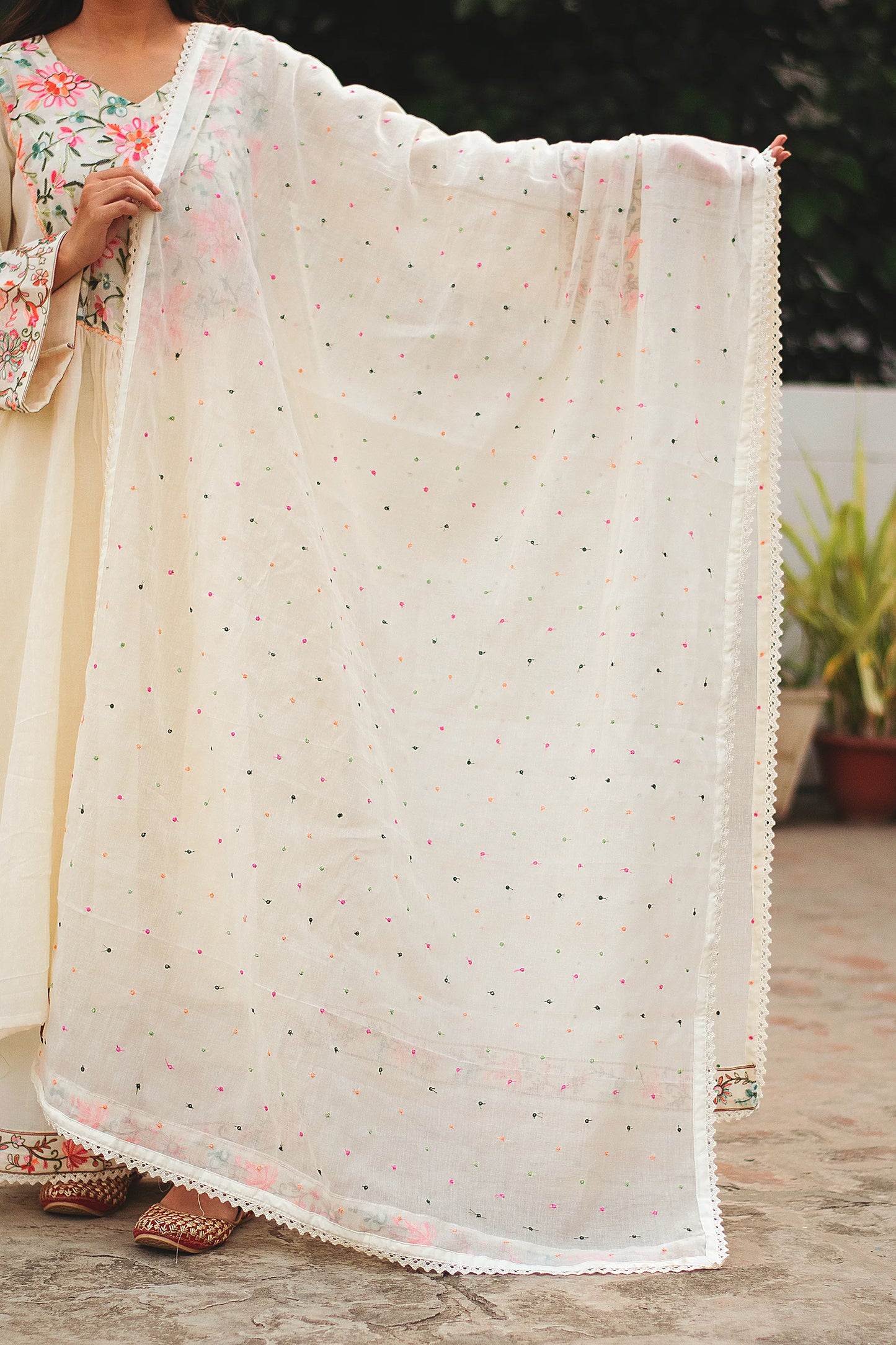 Close-up of an off-white cotton dupatta, featuring intricate Kashmiri embroidery in vibrant hues, draped over the shoulder of a young Indian woman.