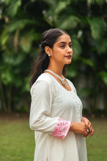  Side view of an Indian model in an off-white chanderi kurta adorned with pink floral cutwork and sequins.