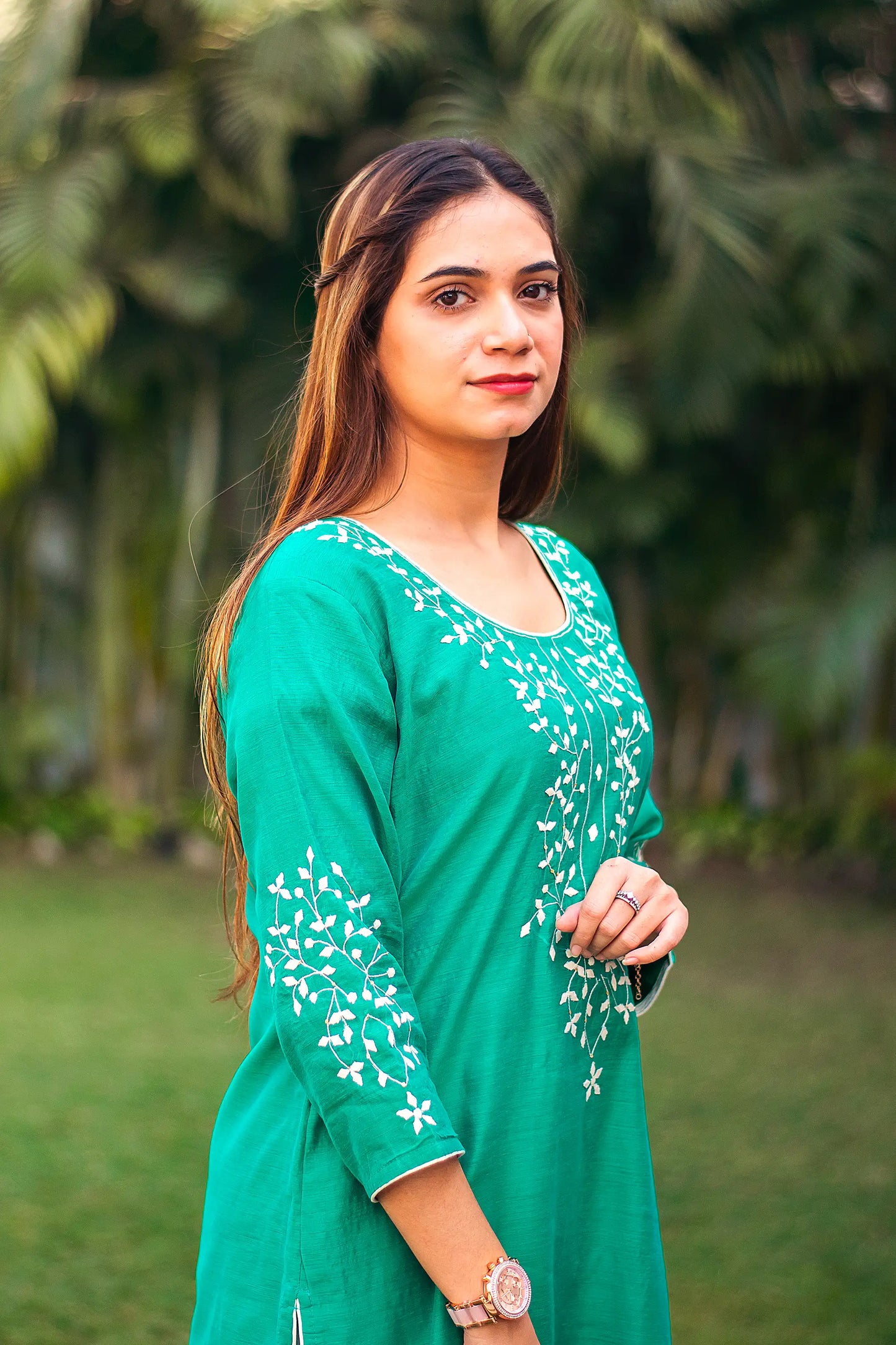 An Indian girl in a right side pose wearing a green Chanderi kurti with applique work, upper half is visible.