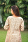 An indian woman wearing a printed staple tussar gold A line kurta and trousers. The A line kurta has double kali in red colour. The woman's back side is facing the camera and the attire is visible from neck till the torso.