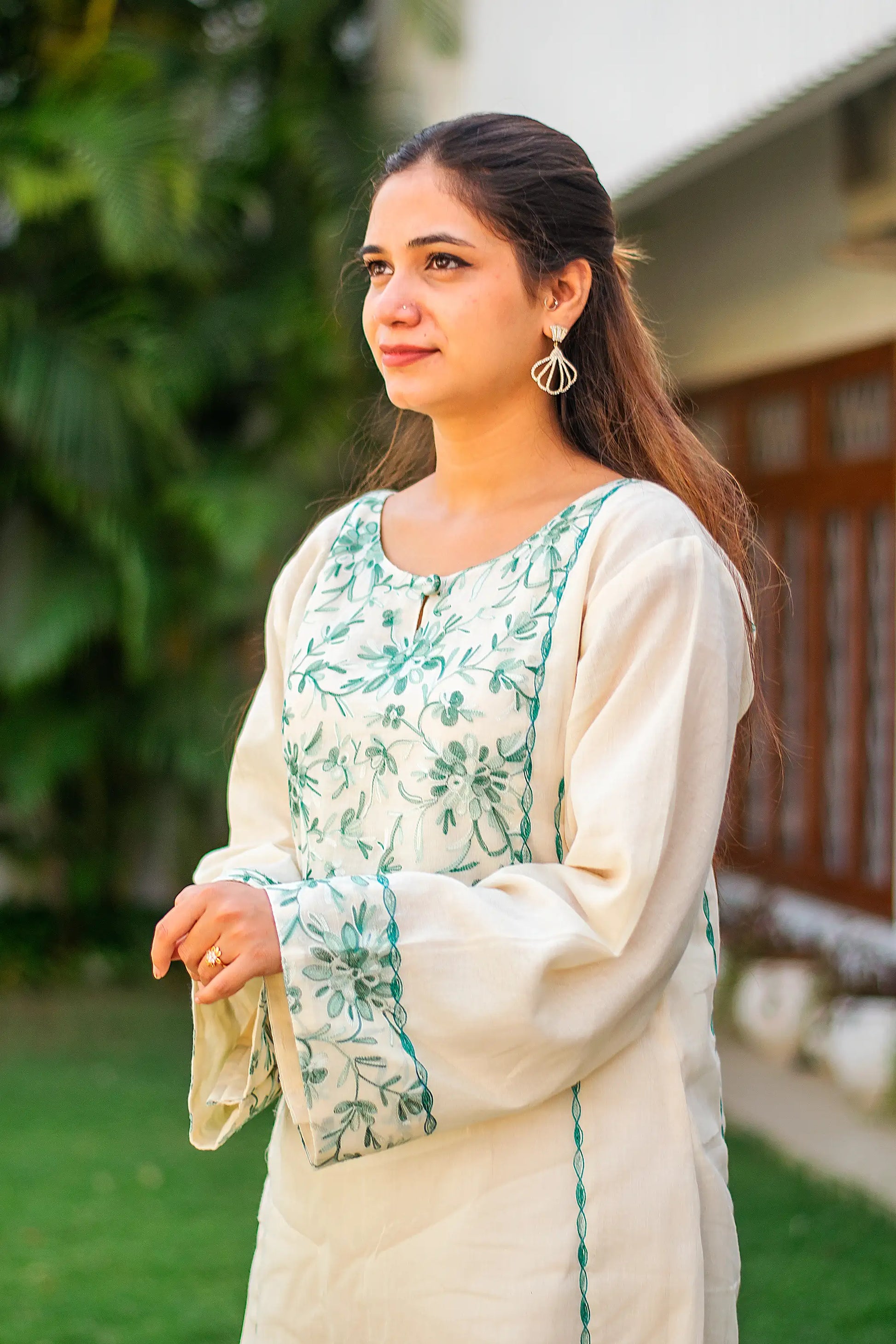 Side view of an Indian model in an off-white kurta with green Kashmiri embroidery.