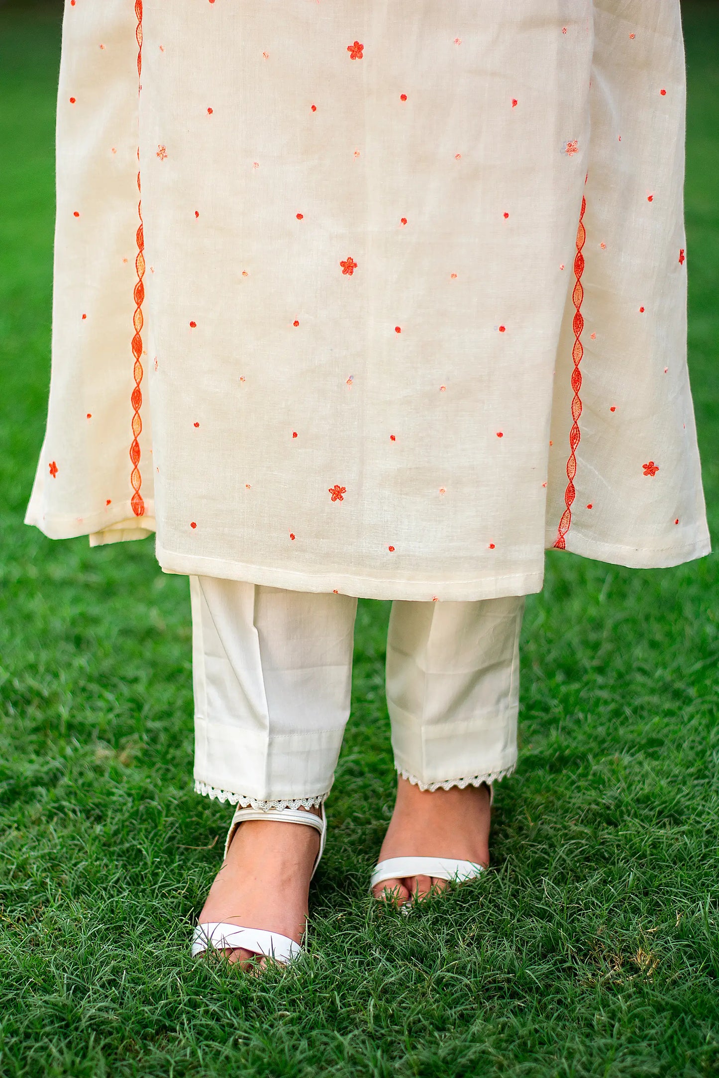 Close-up of an Indian model in plain off-white trousers, part of the peach Kashmiri embroidered kurta set.