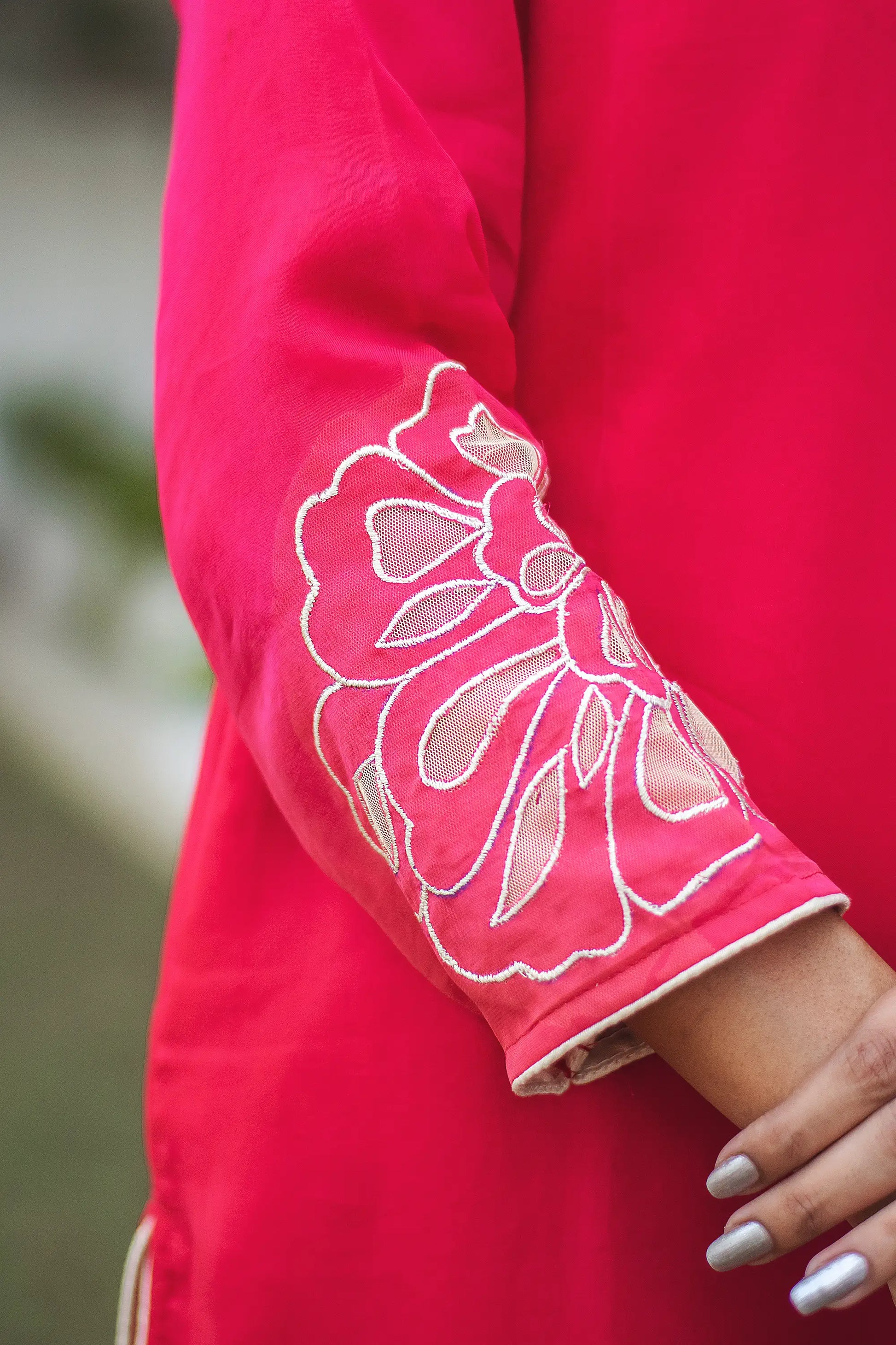 Detailed view of gold floral cutwork on the sleeve of a red organza kurta.