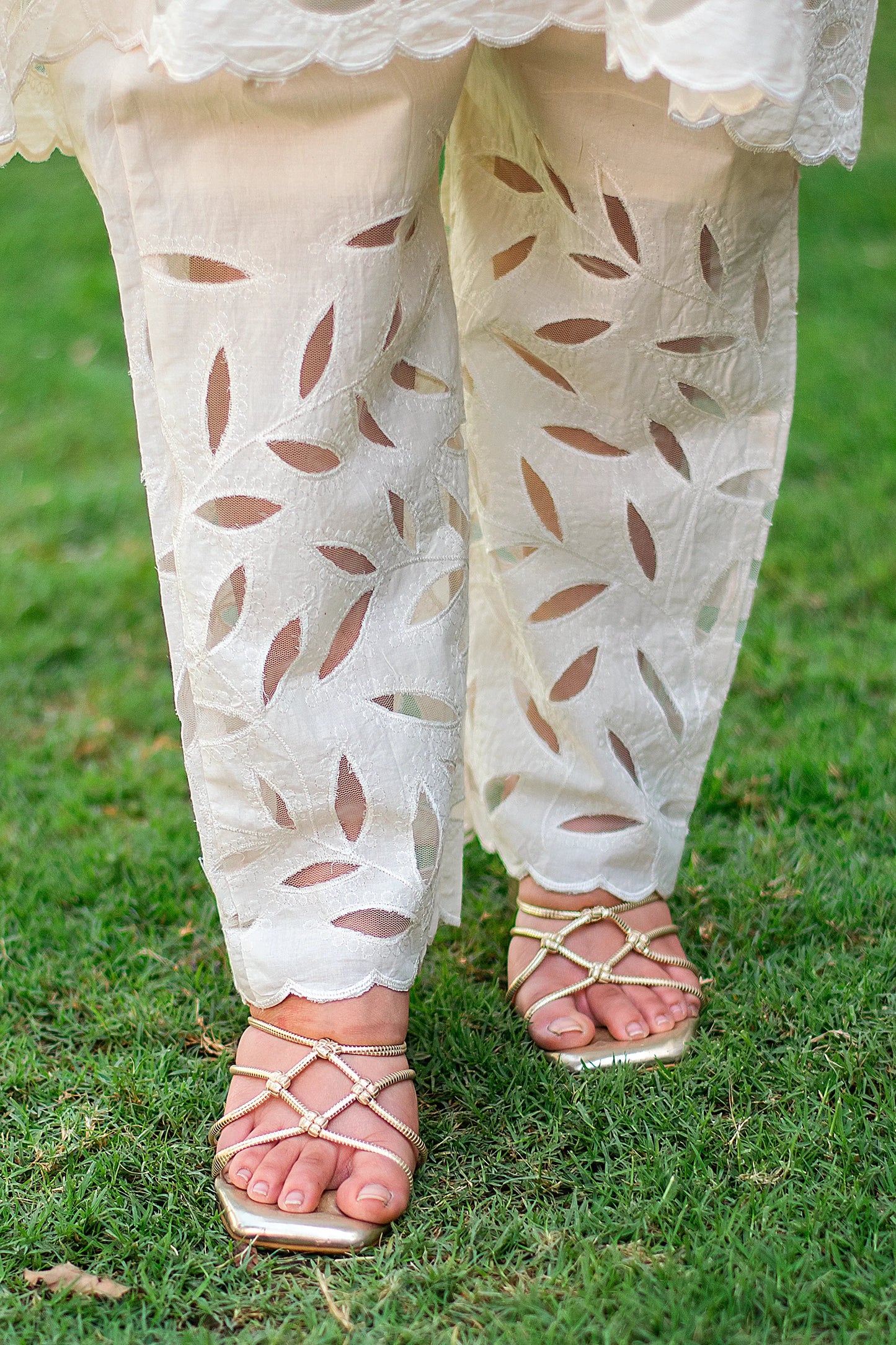 Close-up of the off-white trousers with broad floral cutwork embroidery on the lower half.