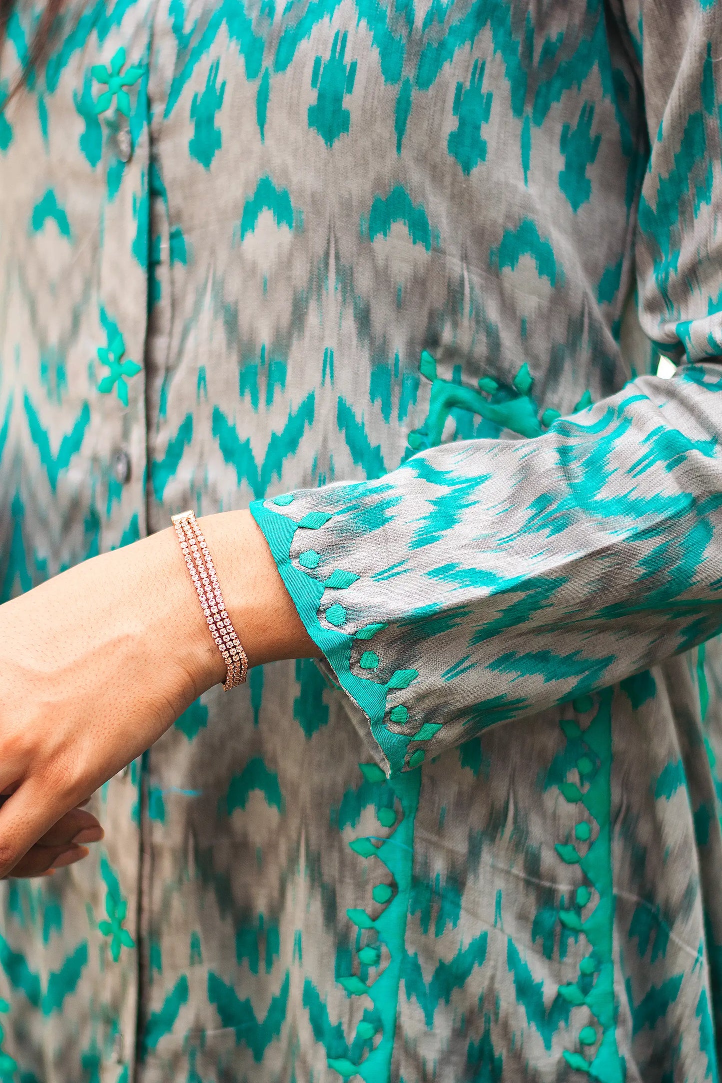 Close-up of the green applique detailing on the sleeve of the grey and green ikat print kurta.