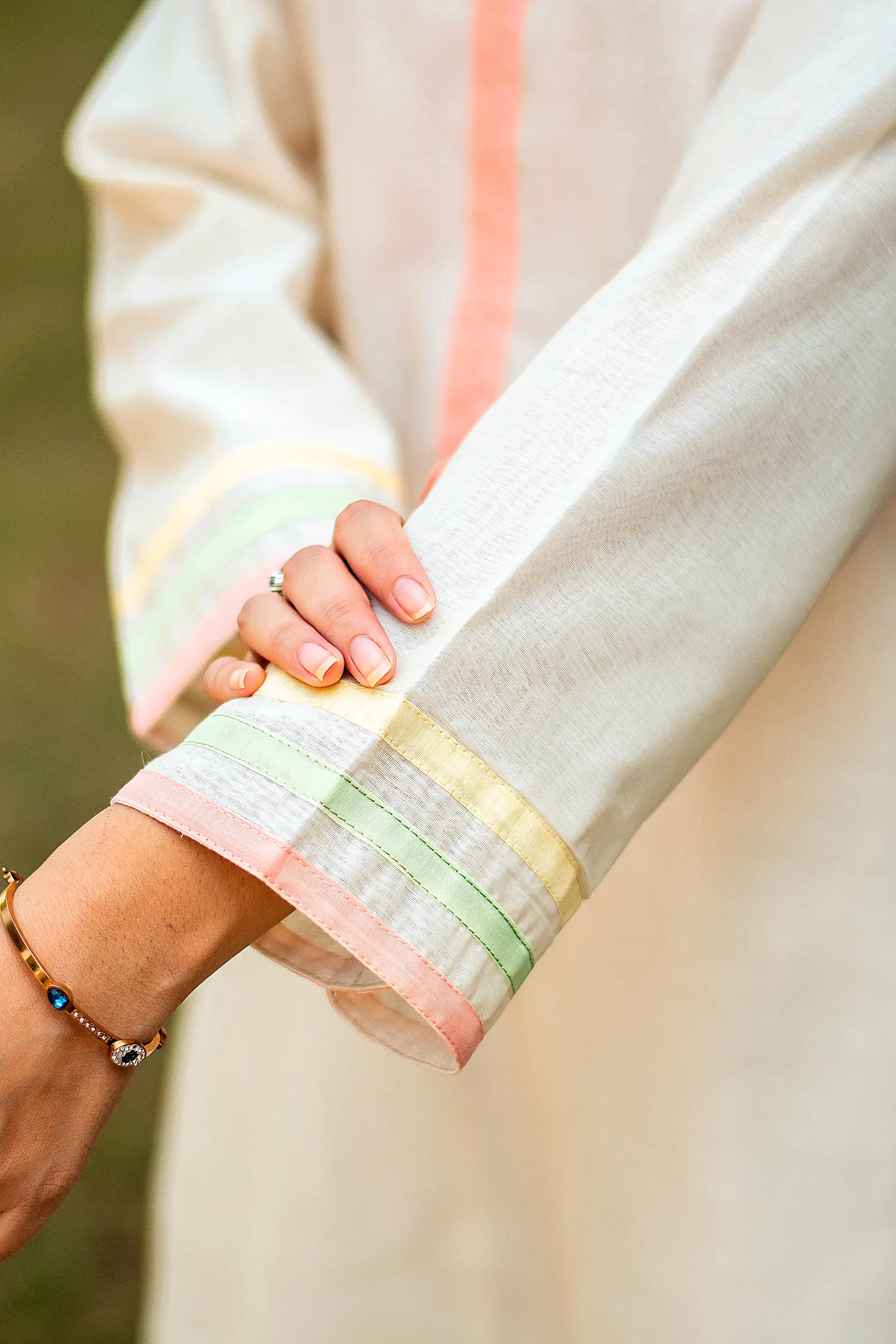 Close-up of the pastel peach, green, and yellow piping on the sleeve of the off-white kurta.