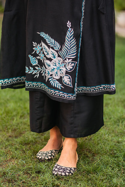 Close-up of the model focusing on the white and blue floral embroidered motif near the hem of the black chanderi angrakha kurta.