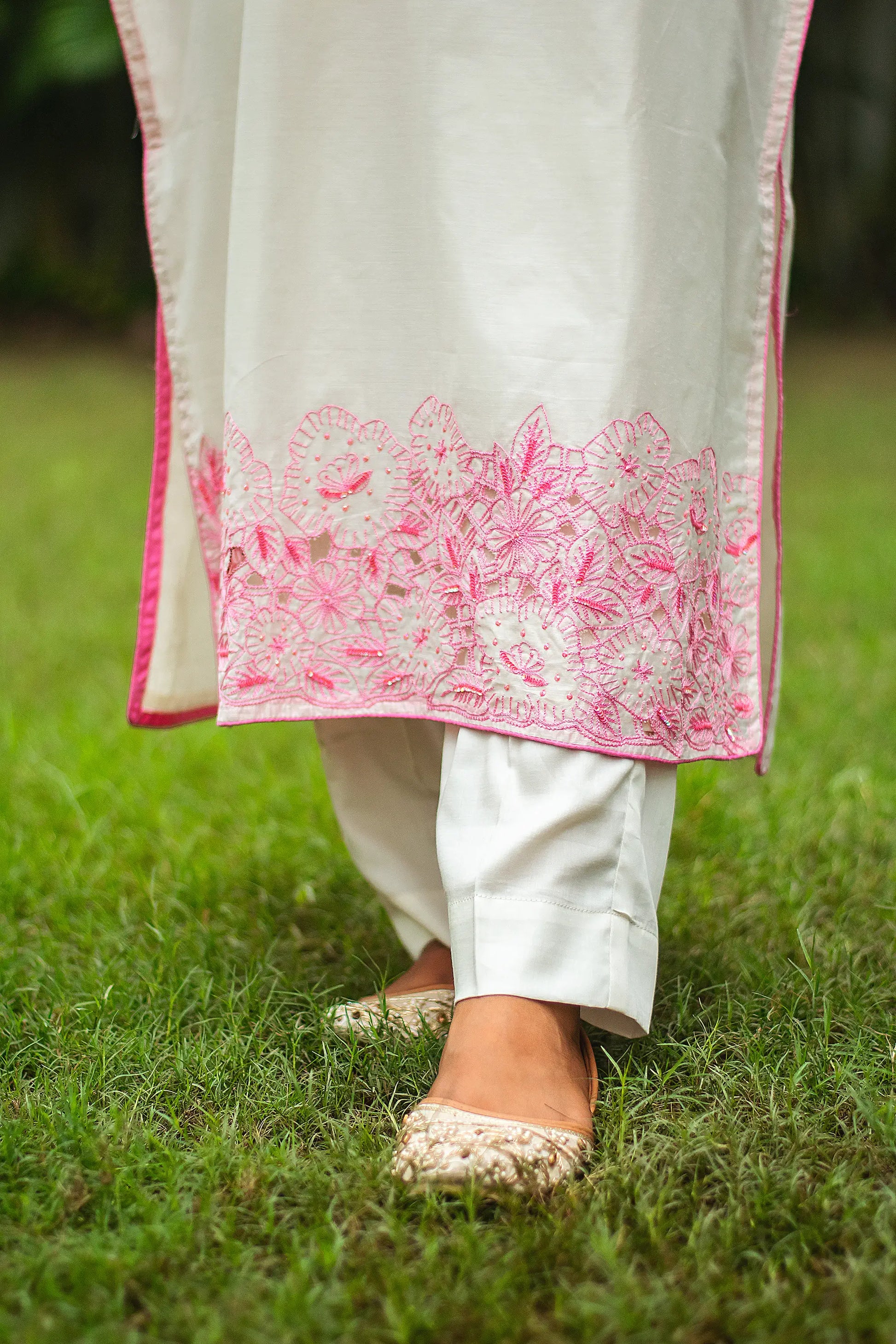 Close-up of the trousers and hem of the off-white chanderi kurta showing intricate pink floral cutwork and sequins.