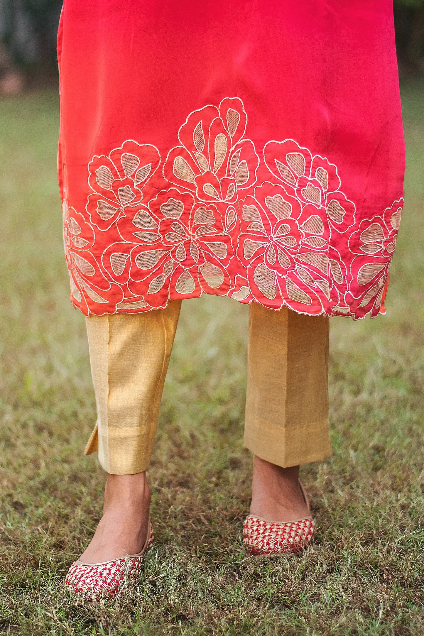 Zoomed-in shot highlighting the gold cutwork along the hem of a red organza kurta worn by an Indian model.