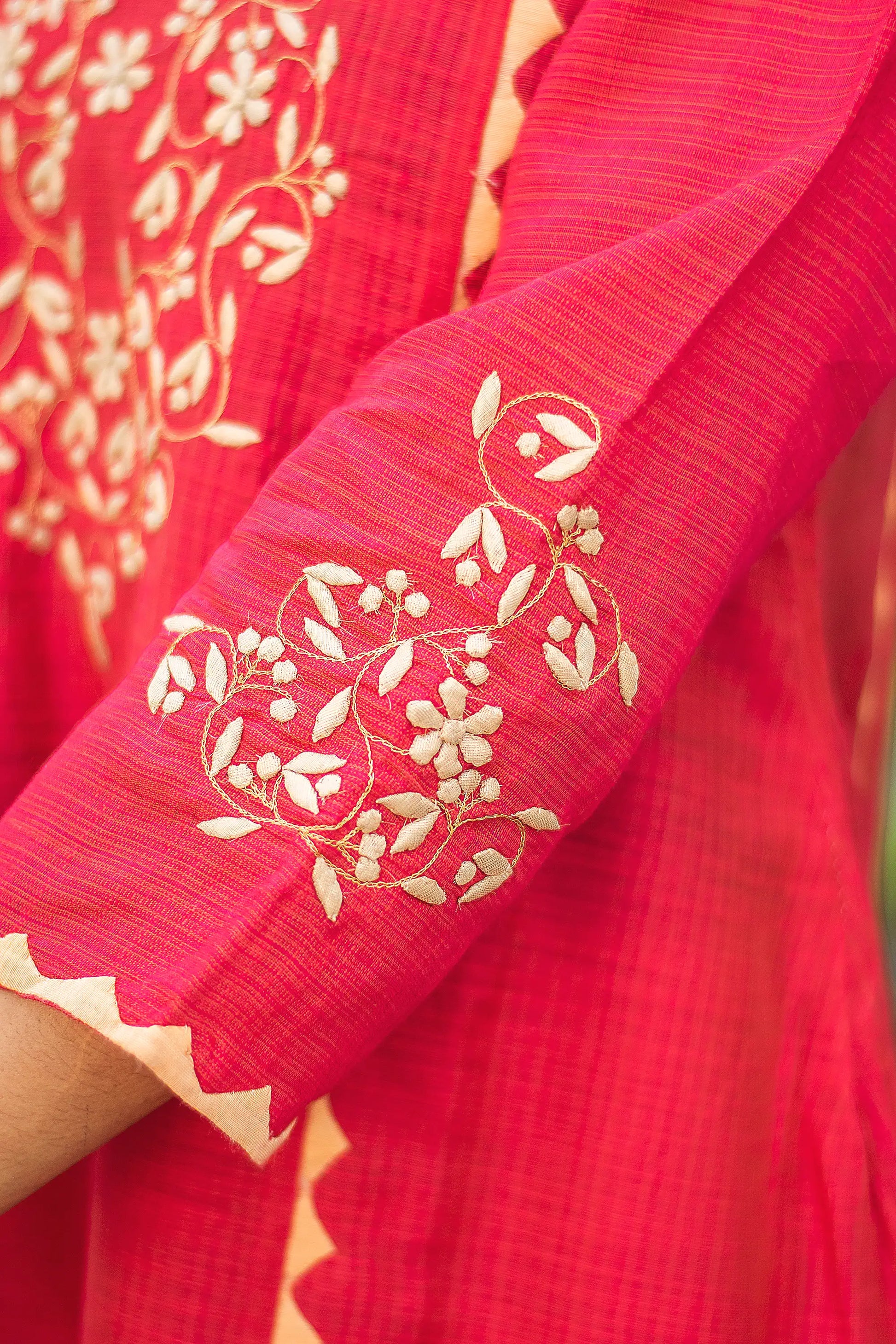 Close-up of the beige applique detailing on the sleeve of the red jute silk kurta.