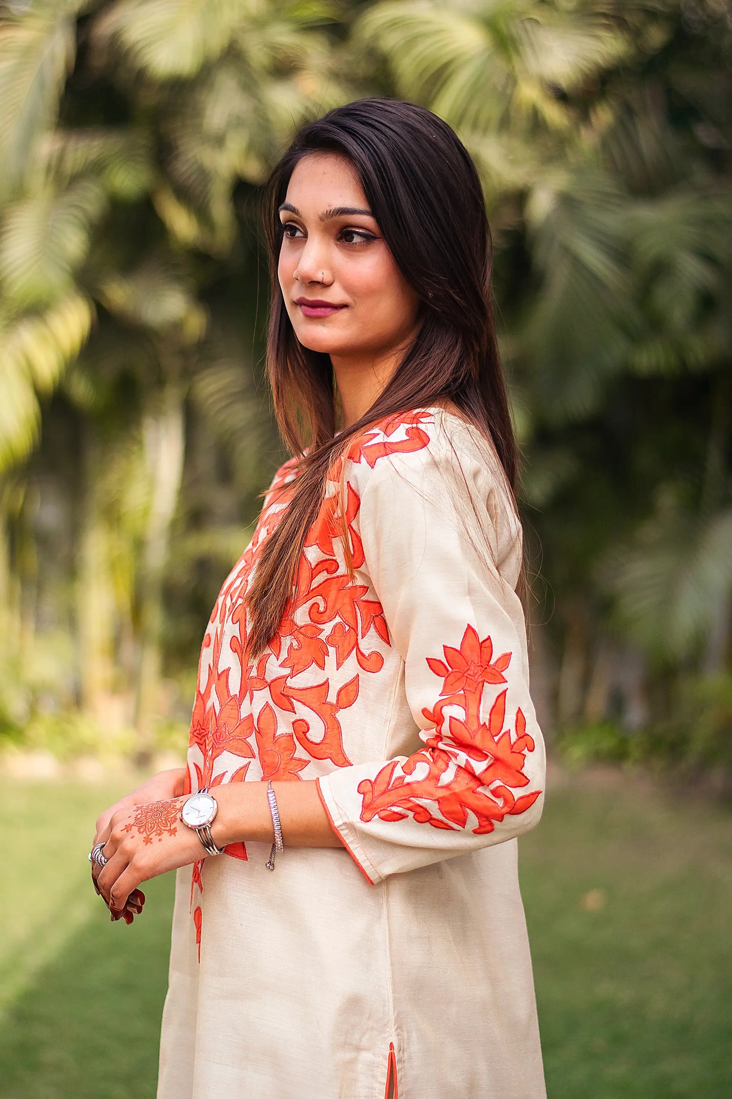 Side view of an Indian model in a beige chanderi kurta with orange floral patchwork around the yoke and cuffs.