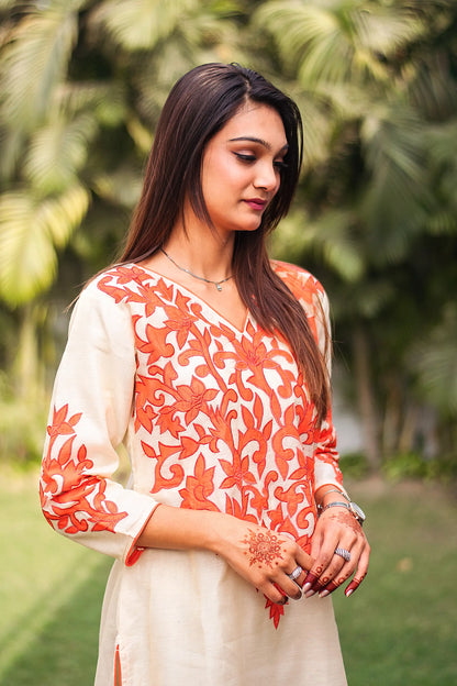 Indian model in a side pose, dressed in the straight-cut silhouette of the beige chanderi kurta with orange patchwork.