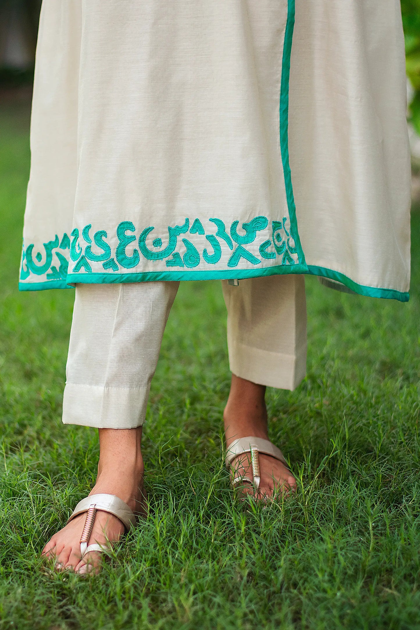 Detailed shot of the green calligraphy patchwork adorning the hem of the beige angrakha, as styled by the model