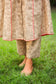 An indian woman wearing a printed staple tussar gold A line kurta and trousers. The A line kurta has double kali in red colour. The woman's front is facing the camera and the camera has zoomed in to focus on the print of the kurta and the trousers.
