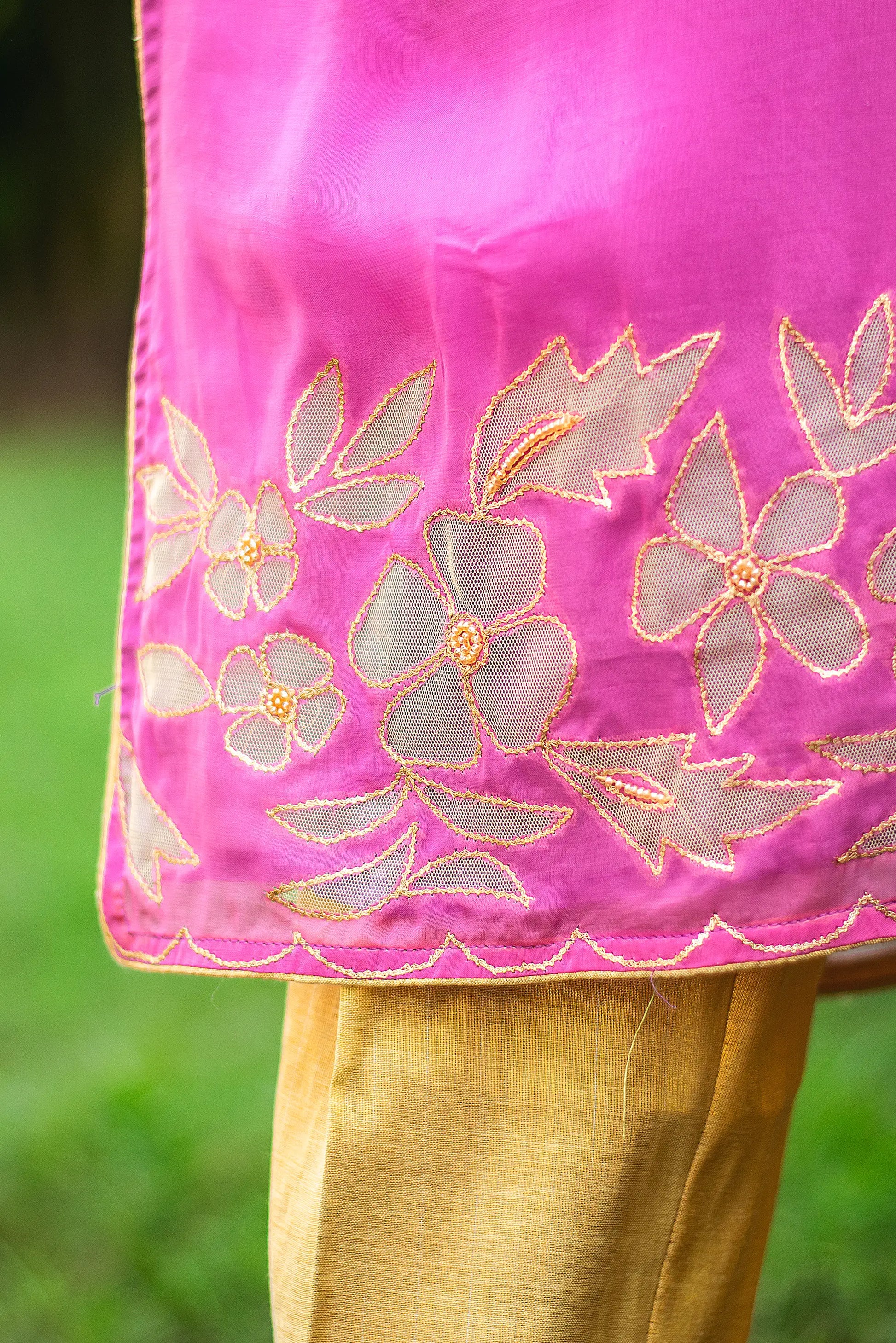 	Zoomed-in view of golden floral cutwork on the hem of a light purple organza kurta.