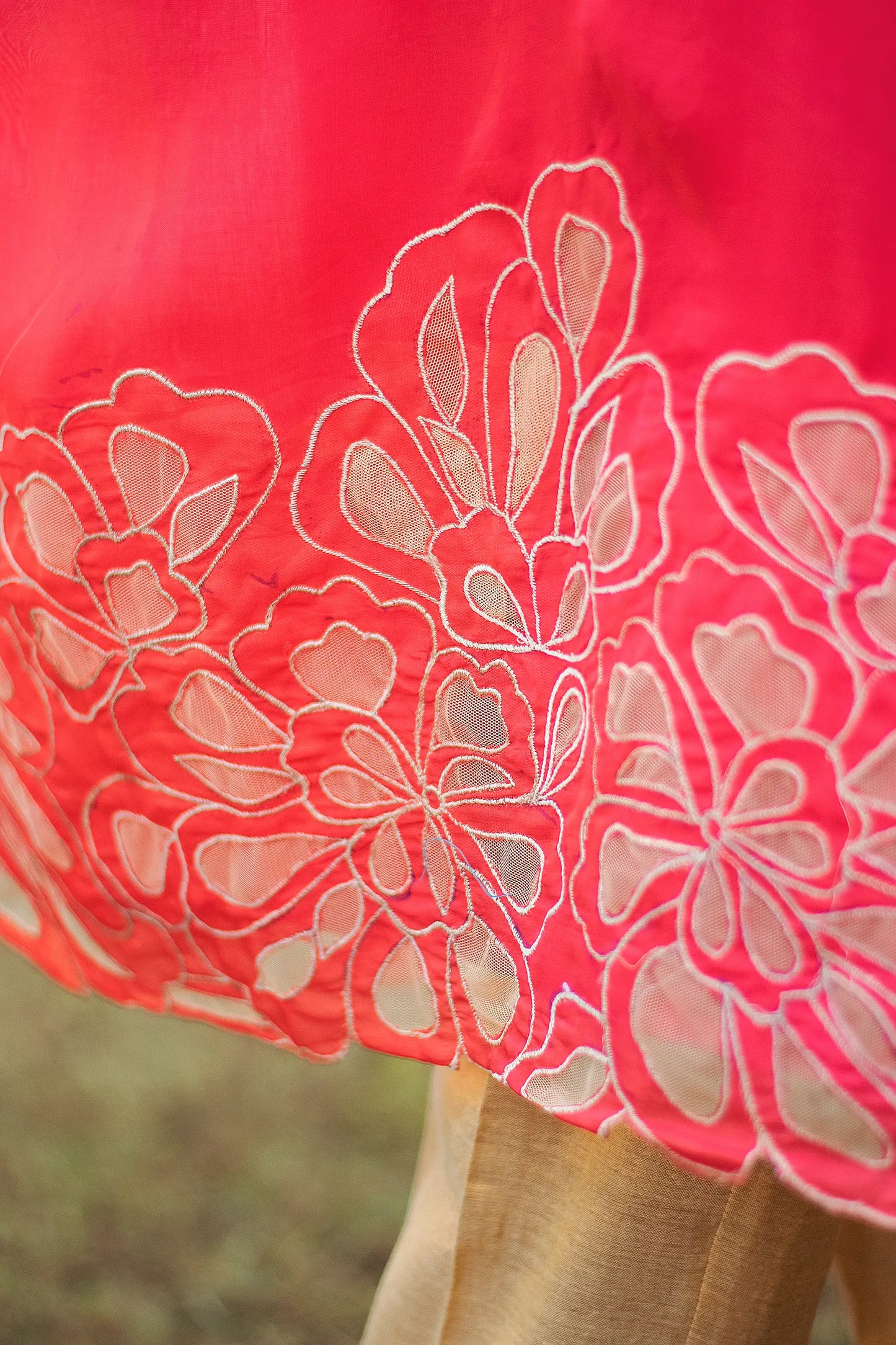 Close-up of gold floral cutwork along the hem of a red organza kurta.