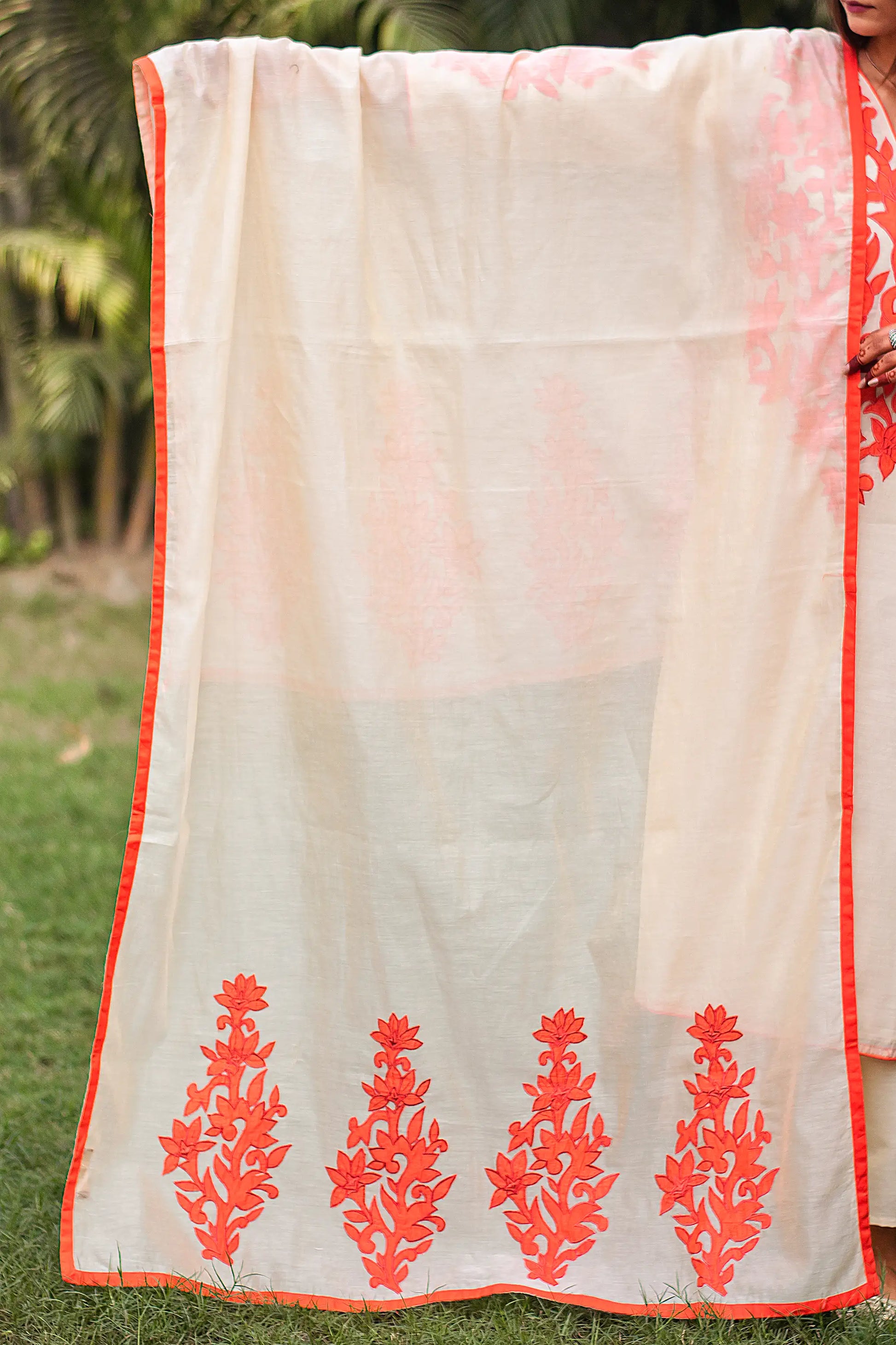 Indian model holding a beige chanderi dupatta with thick orange patchwork paisleys and orange trimming along the border.