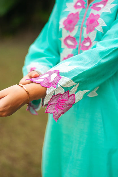 Close-up of purple patchwork flowers on the sleeve of a blue chanderi kurta with pink piping.