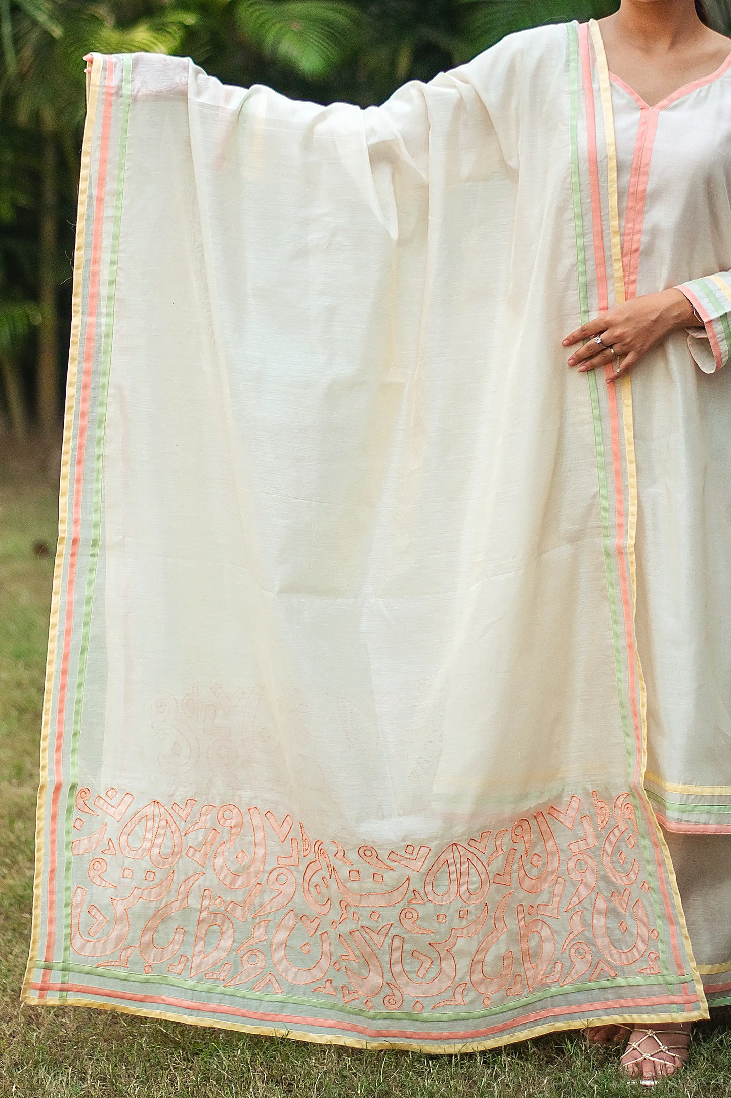 Indian model holding an off-white chanderi dupatta with pastel-colored patchwork motifs and piping.