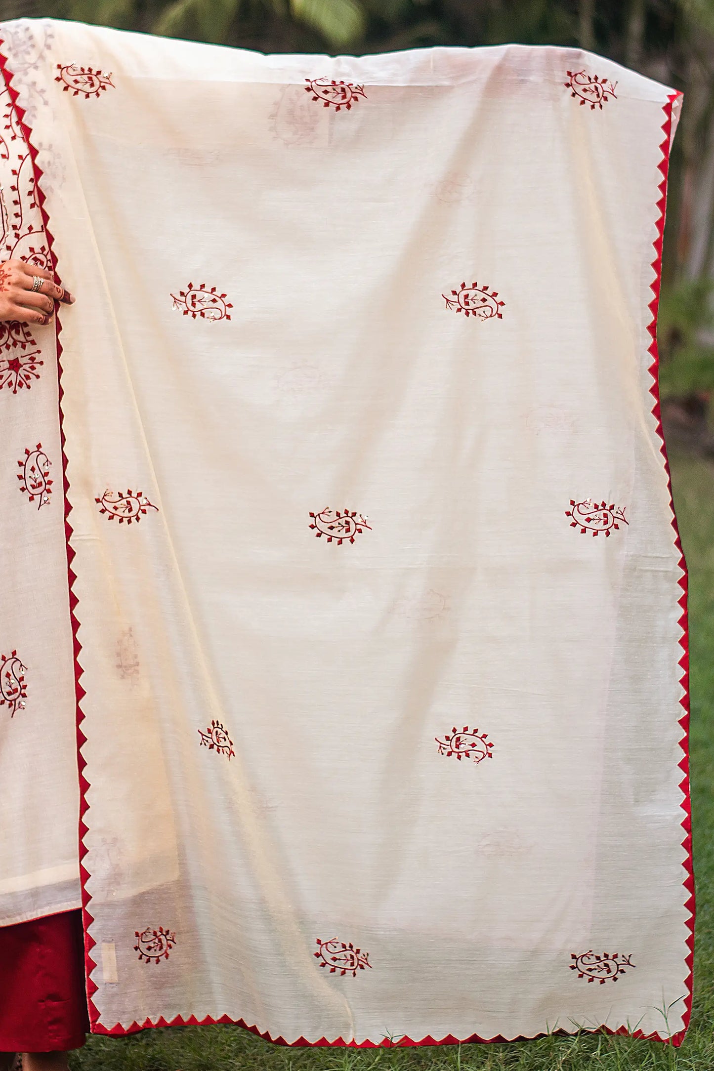 Indian model holding a beige chanderi dupatta with maroon paisley applique motifs and maroon kikri detailing along the border.