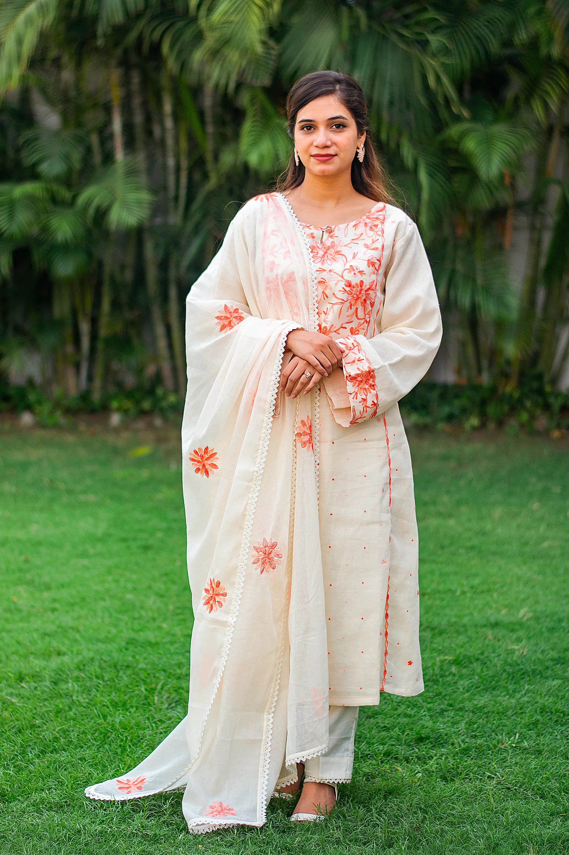 Indian model in an off-white kurta with peach Kashmiri embroidery, paired with a matching dupatta and trousers. 