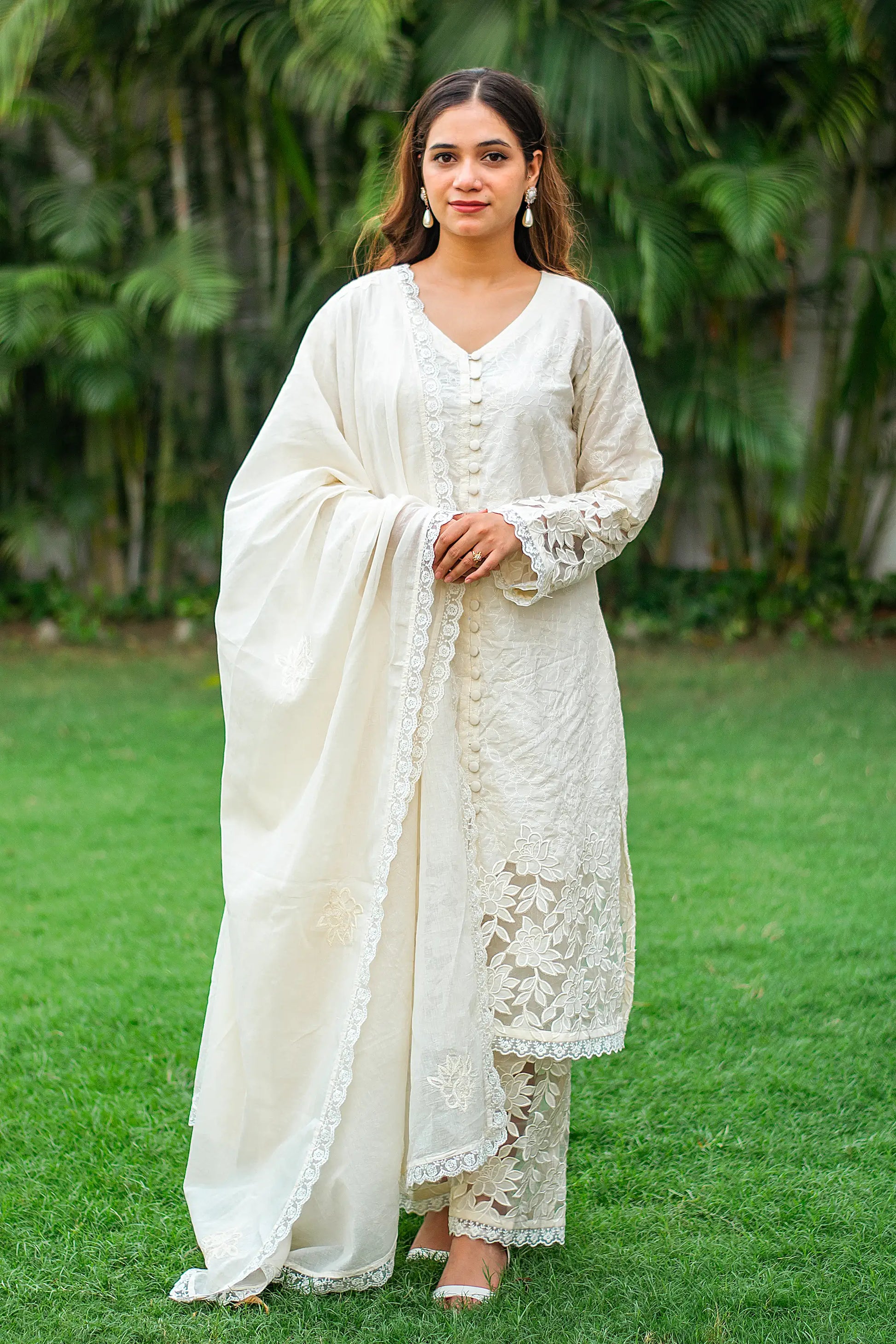 Indian model wearing a white cotton kurta,dupatta and trousers with floral cutwork. 