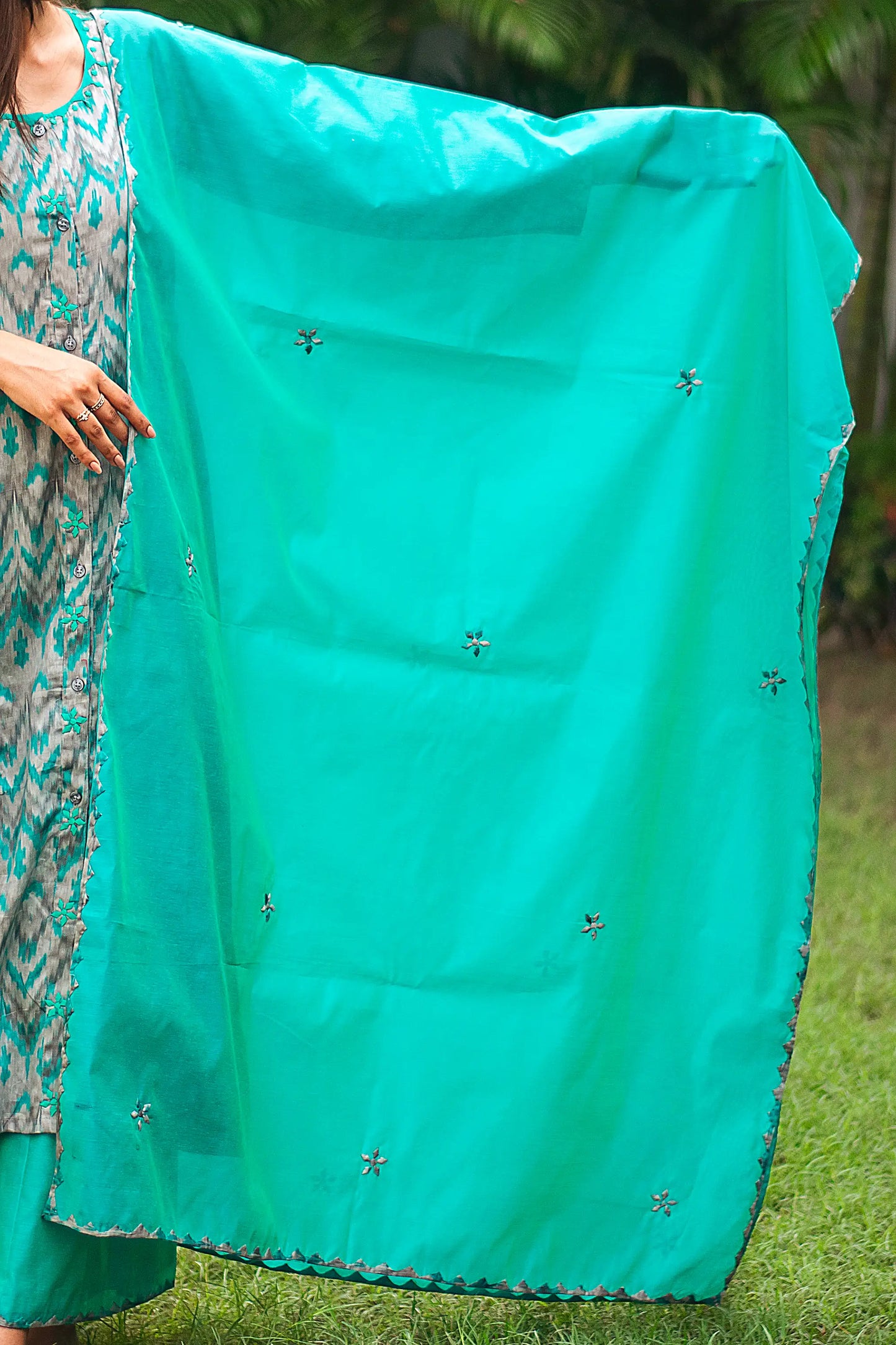 Indian model holding a green chanderi dupatta with intricate applique kikri motifs and delicate applique flowers scattered across the fabric.