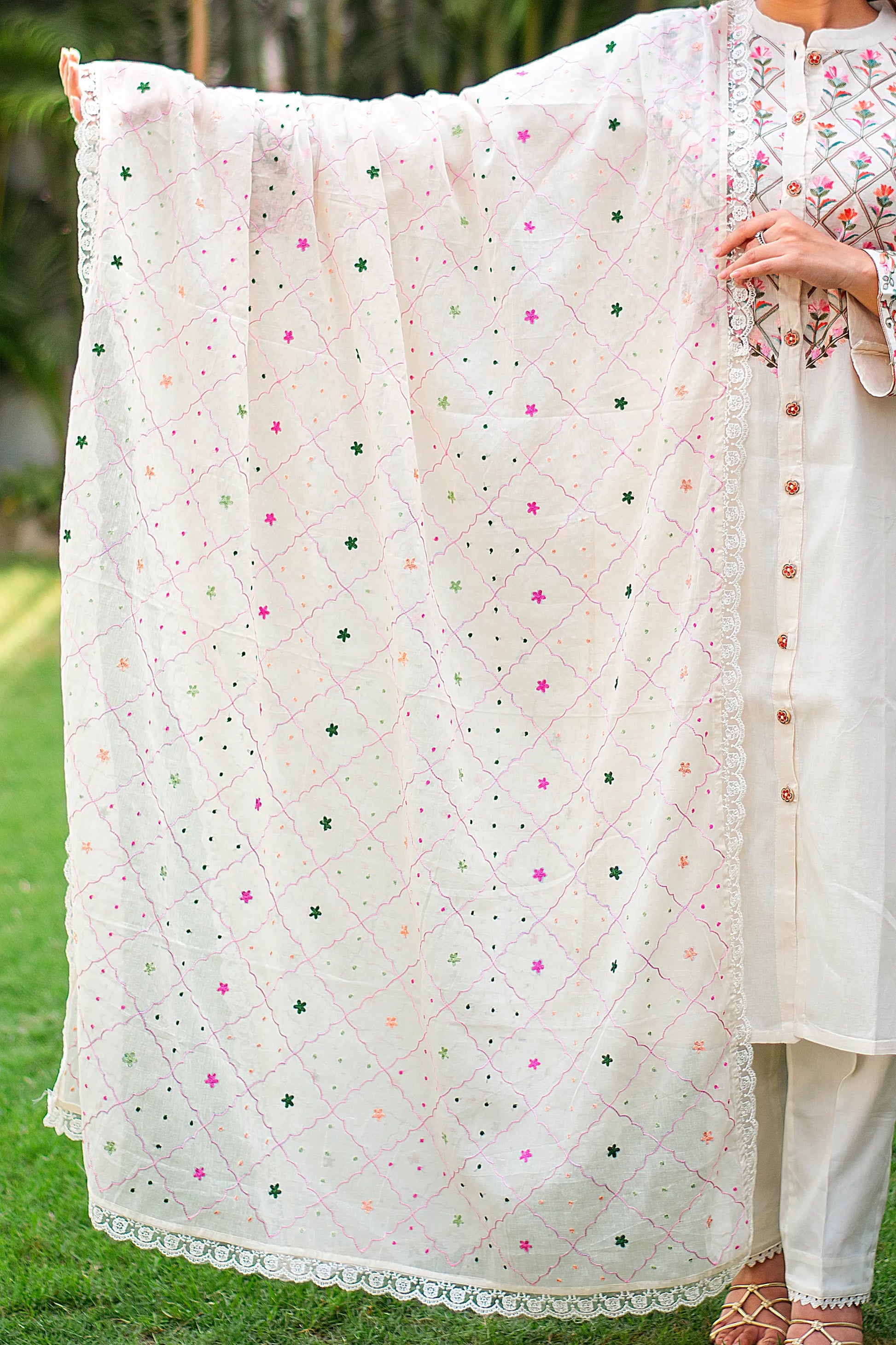 Indian girl holding an off-white dupatta with hand-embroidered peach, pink, and green dots and floral patterns.