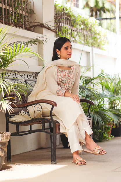 Indian model wearing an off-white Kashmiri embroidered kurta set with cotton kurta, dupatta, and trousers while she sits on a bench