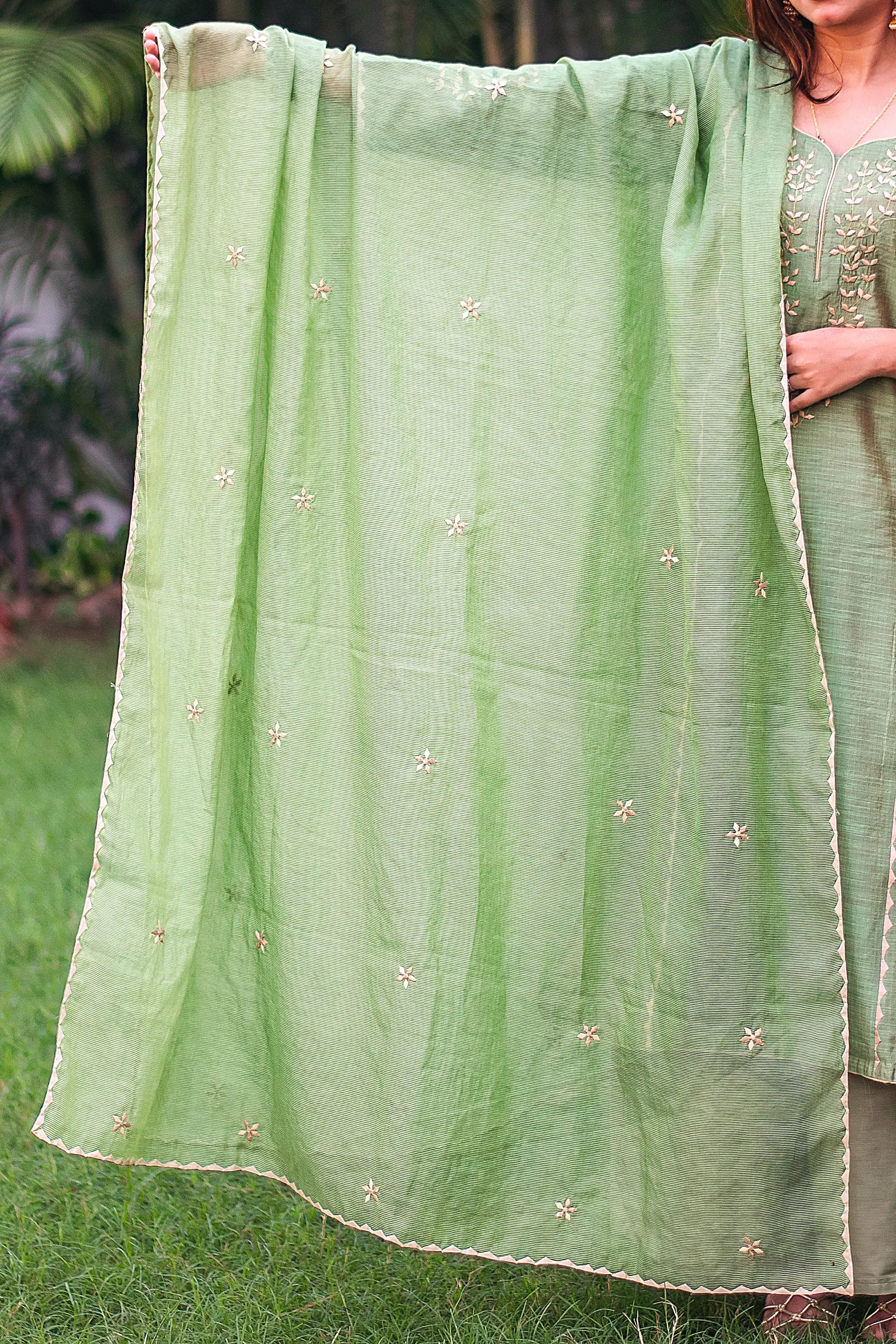 Indian model holding a green chanderi dupatta adorned with beige floral applique motifs and kikri detailing.