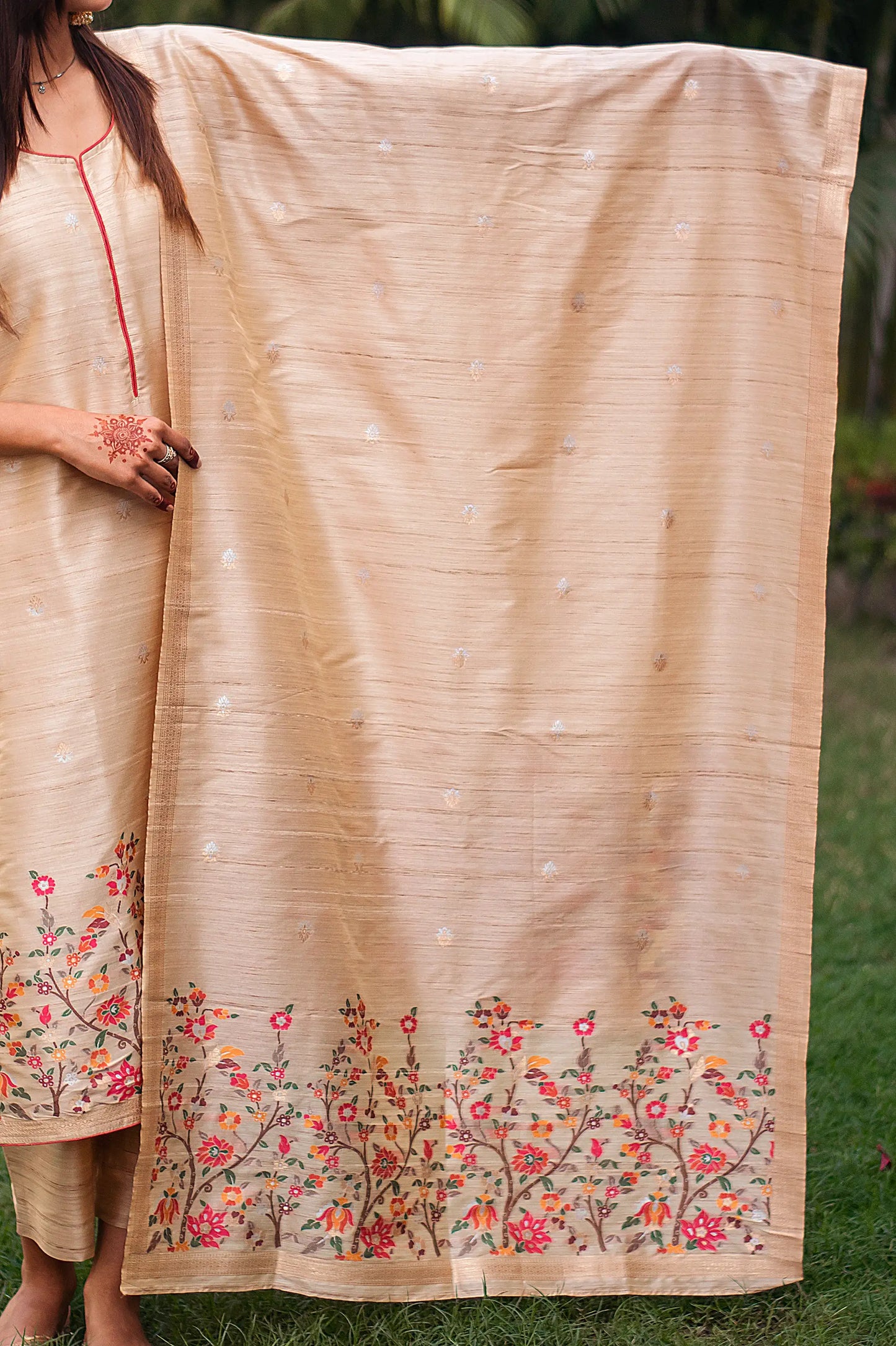 Indian model holding a beige silk dupatta with thick resham floral border and banarasi woven motifs.