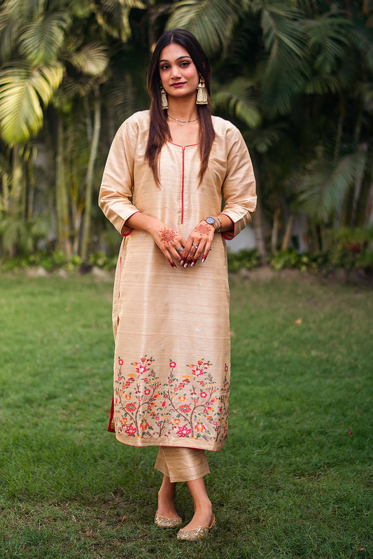 Indian model in a beige silk kurta with vibrant resham weave, paired with matching beige trousers.