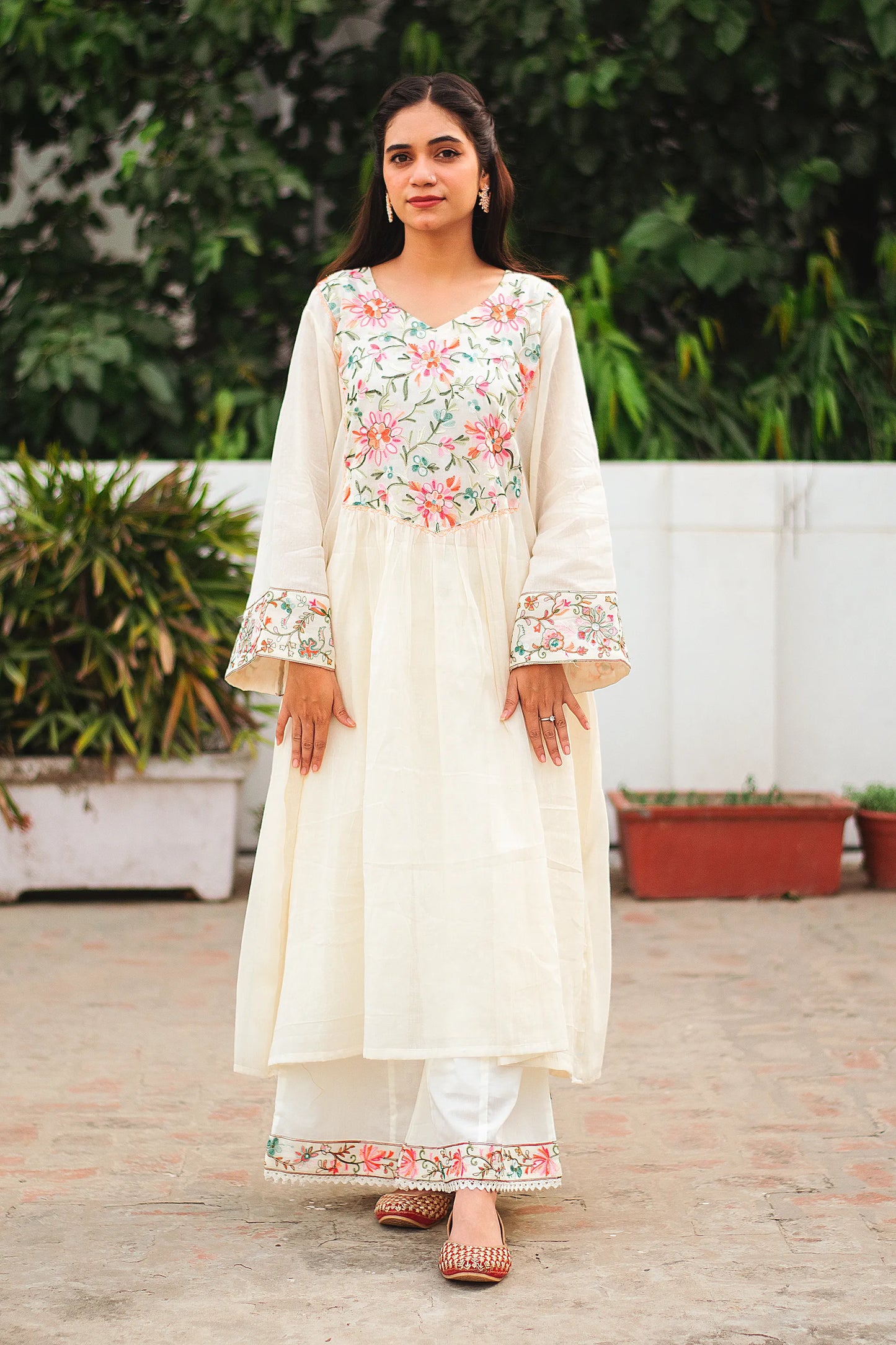 Full body shot of a young Indian woman in an off-white cotton Bahaar-e-Chinaar frock kurta set with matching palazzo pants and dupatta.