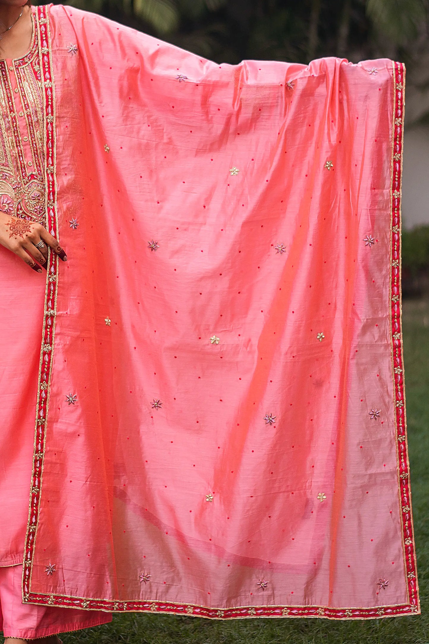 Indian model holding a peach chanderi dupatta with small zardozi flowers and red lace along the borders.