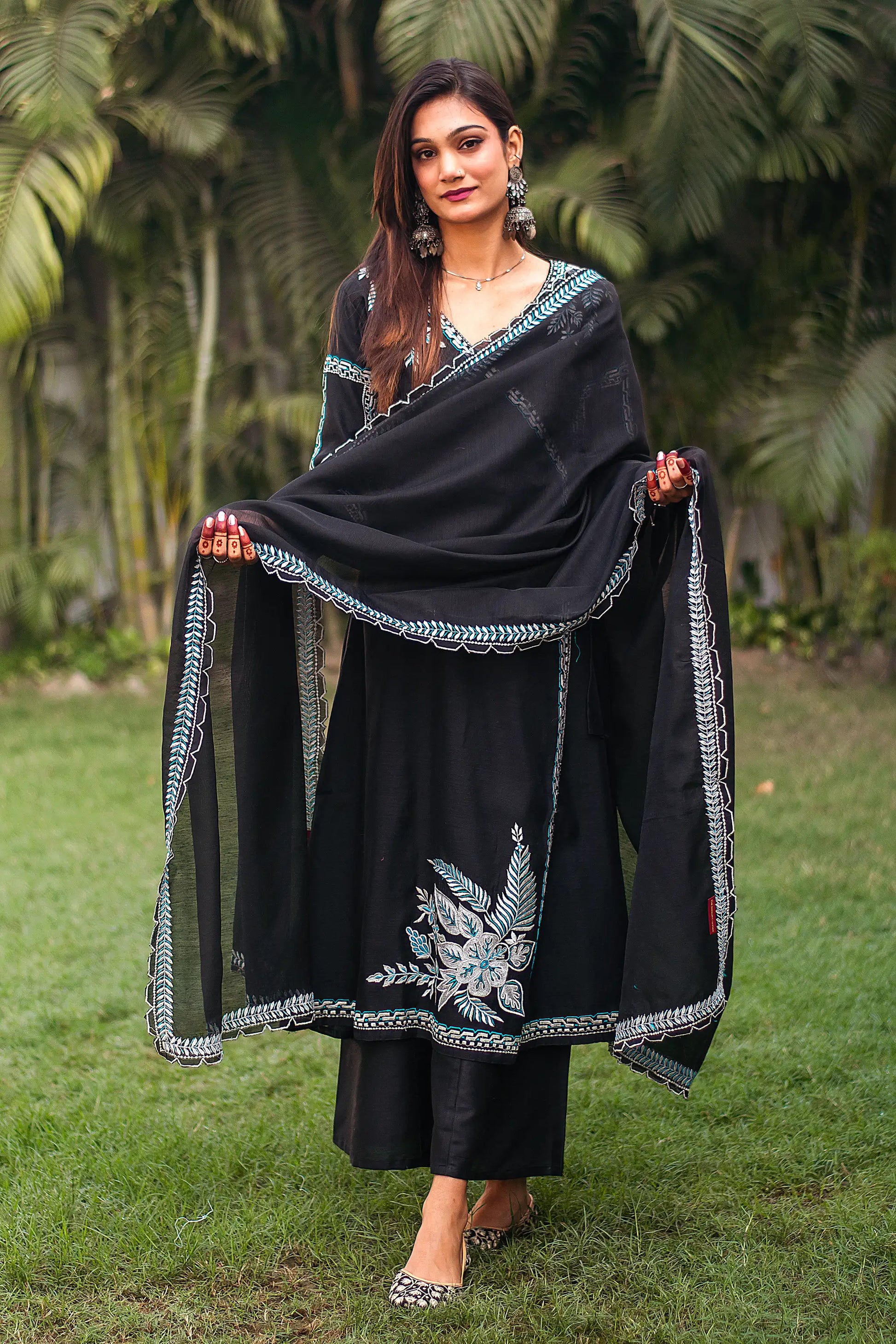 Indian model dressed in a black chanderi angrakha and dupatta with white and blue resham embroidery, paired with matching palazzo.