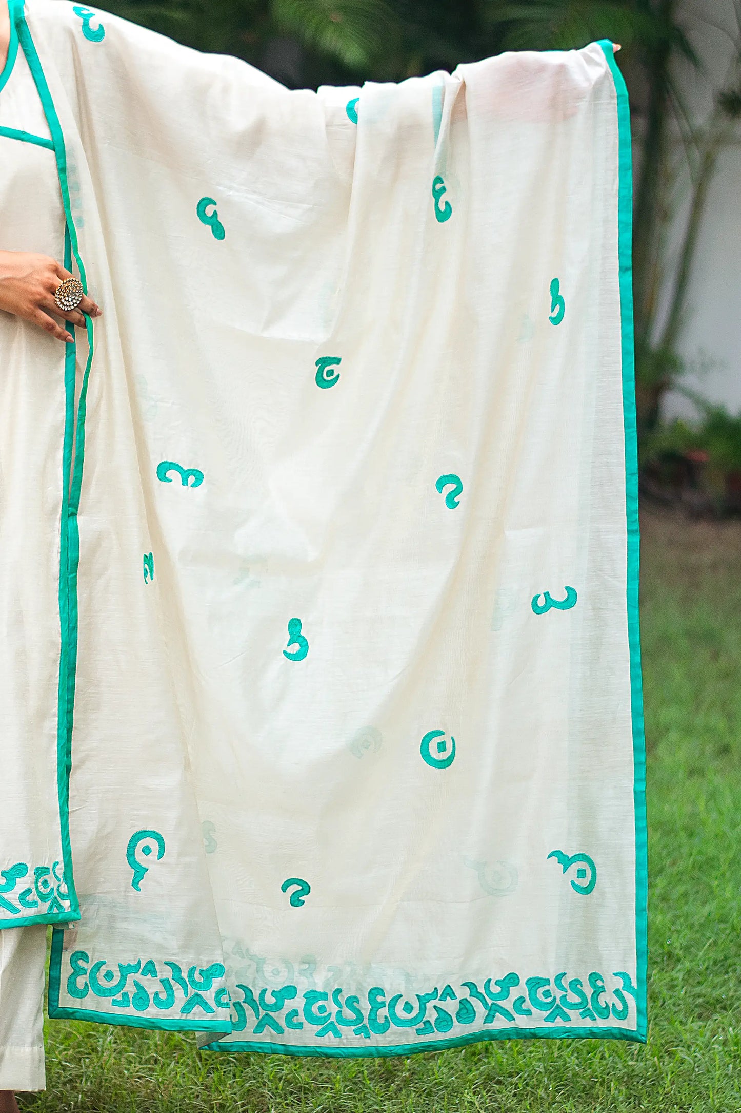 Detail of the beige chanderi dupatta adorned with green calligraphy patchwork running along its borders and scattered across the entire dupatta, as styled by the mode