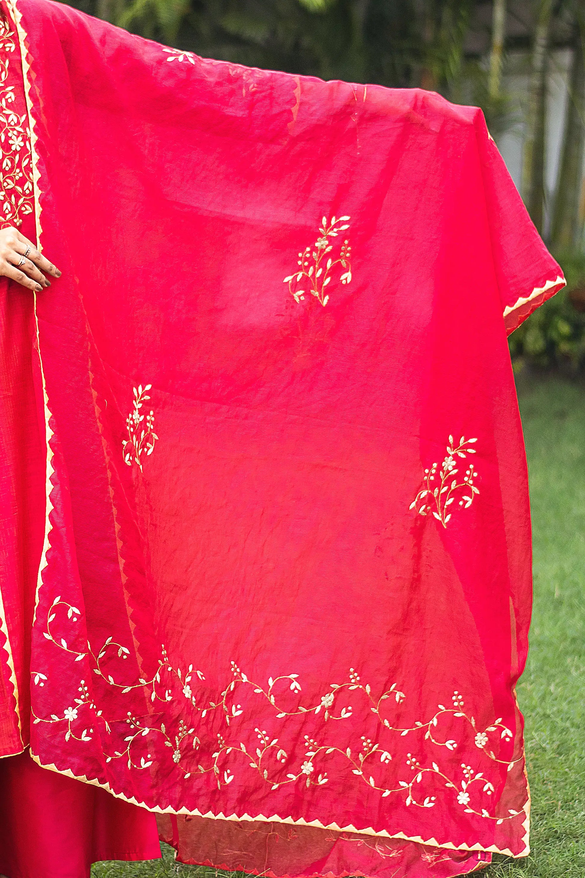 Indian model holding a red chanderi dupatta with beige floral applique motifs and kikri detailing.