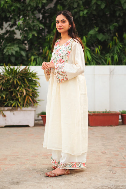 A young Indian woman stands in a side pose, showcasing an off-white cotton Bahaar-e-Chinaar frock kurta set with matching palazzo pants and dupatta.