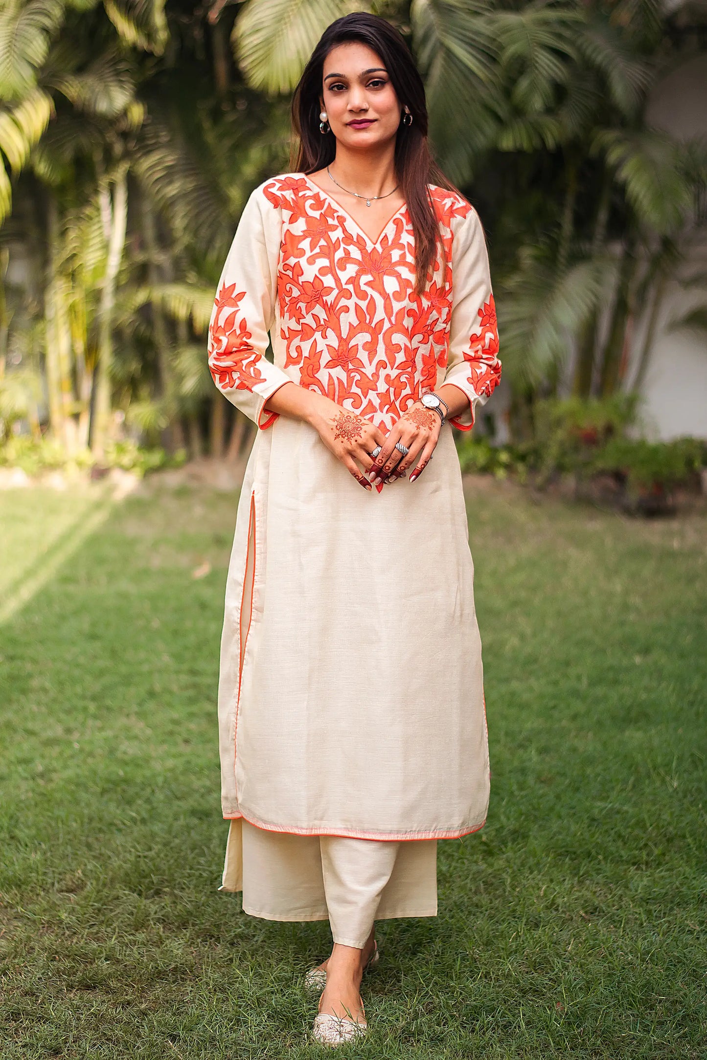 Indian model in a beige chanderi kurta with orange floral patchwork around the yoke and cuffs, paired with matching beige palazzo.