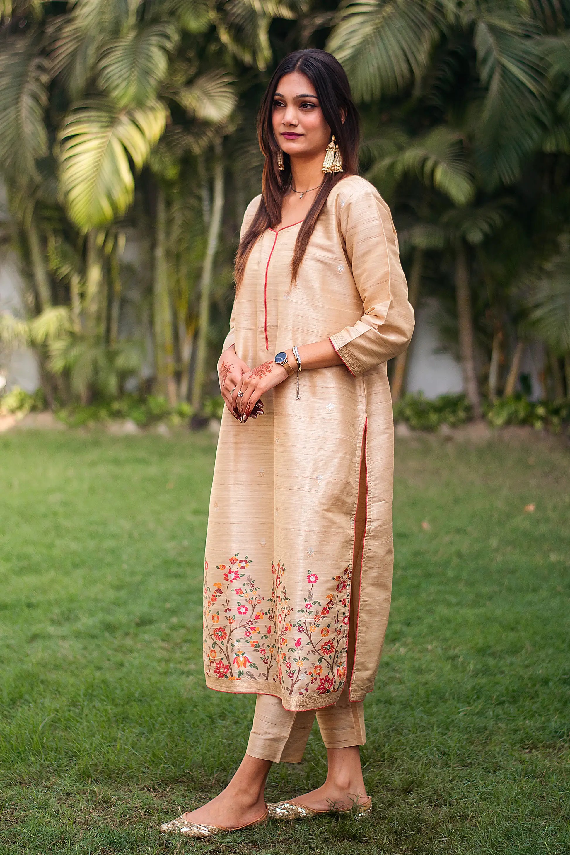 Side view of an Indian model in a beige silk kurta with resham floral border, paired with beige trousers.