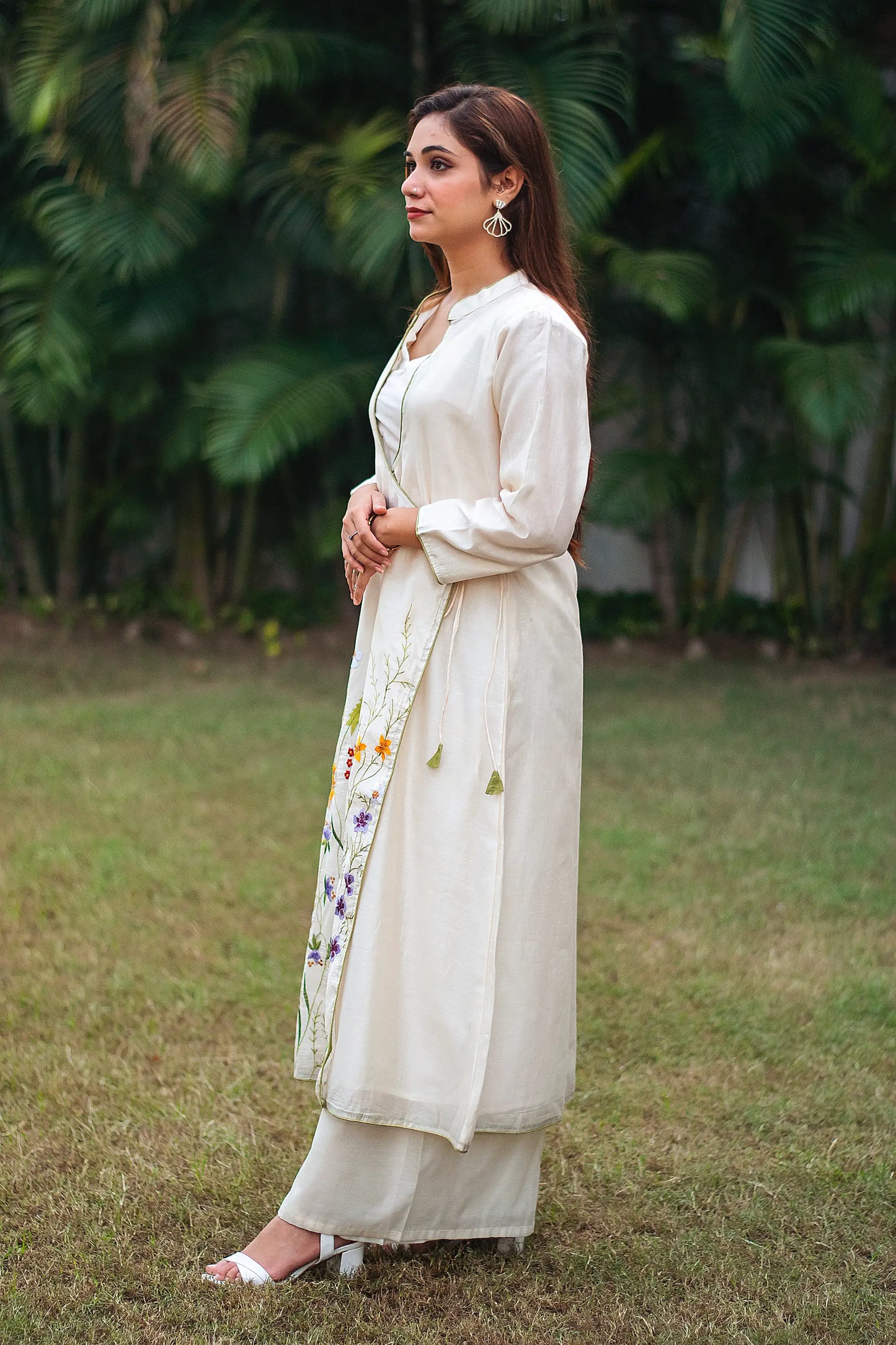 Indian model posing sideways in an off-white angrakha with resham embroidery and off-white palazzo.