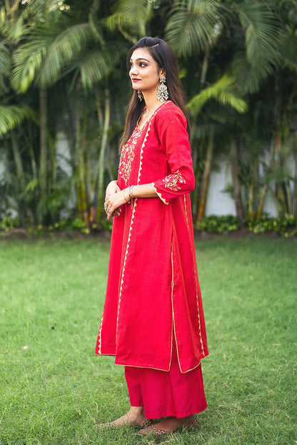 Indian model gives a side pose in a red jute silk kalidar  kurta with beige applique work and a red palazzo