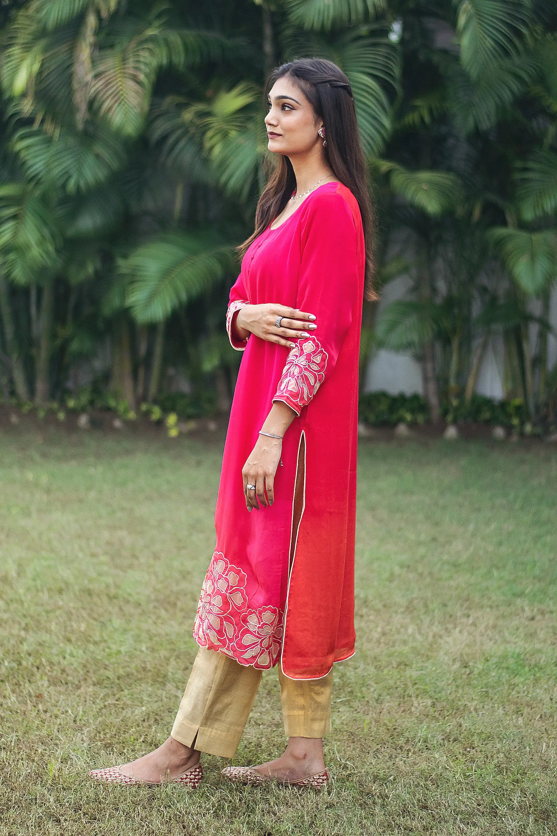 Indian model in a side pose, wearing a red organza kurta with intricate gold cutwork, paired with gold trousers.