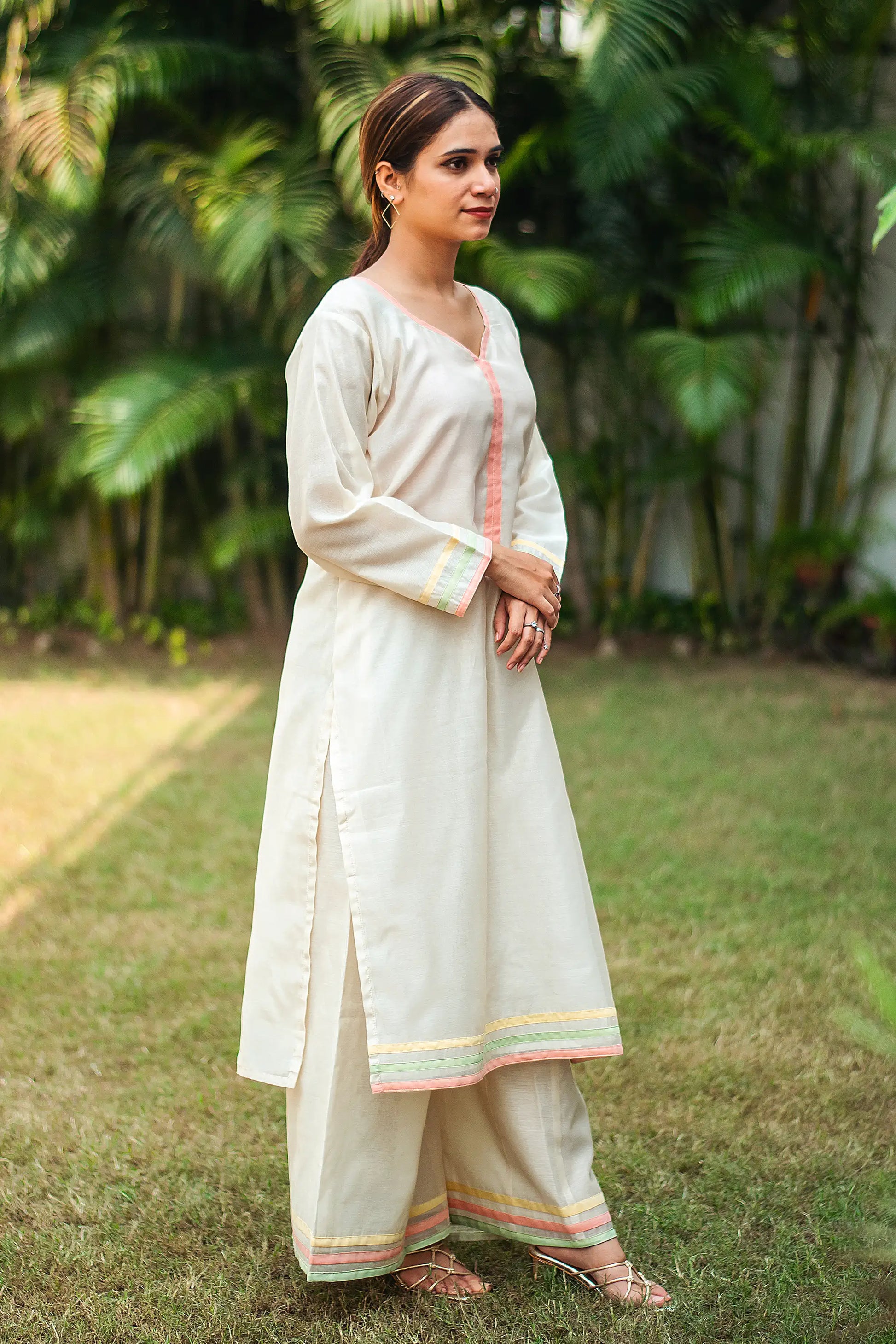 1) Side view of an Indian model in an off-white chanderi kurta with pastel piping, paired with matching off-white palazzo.