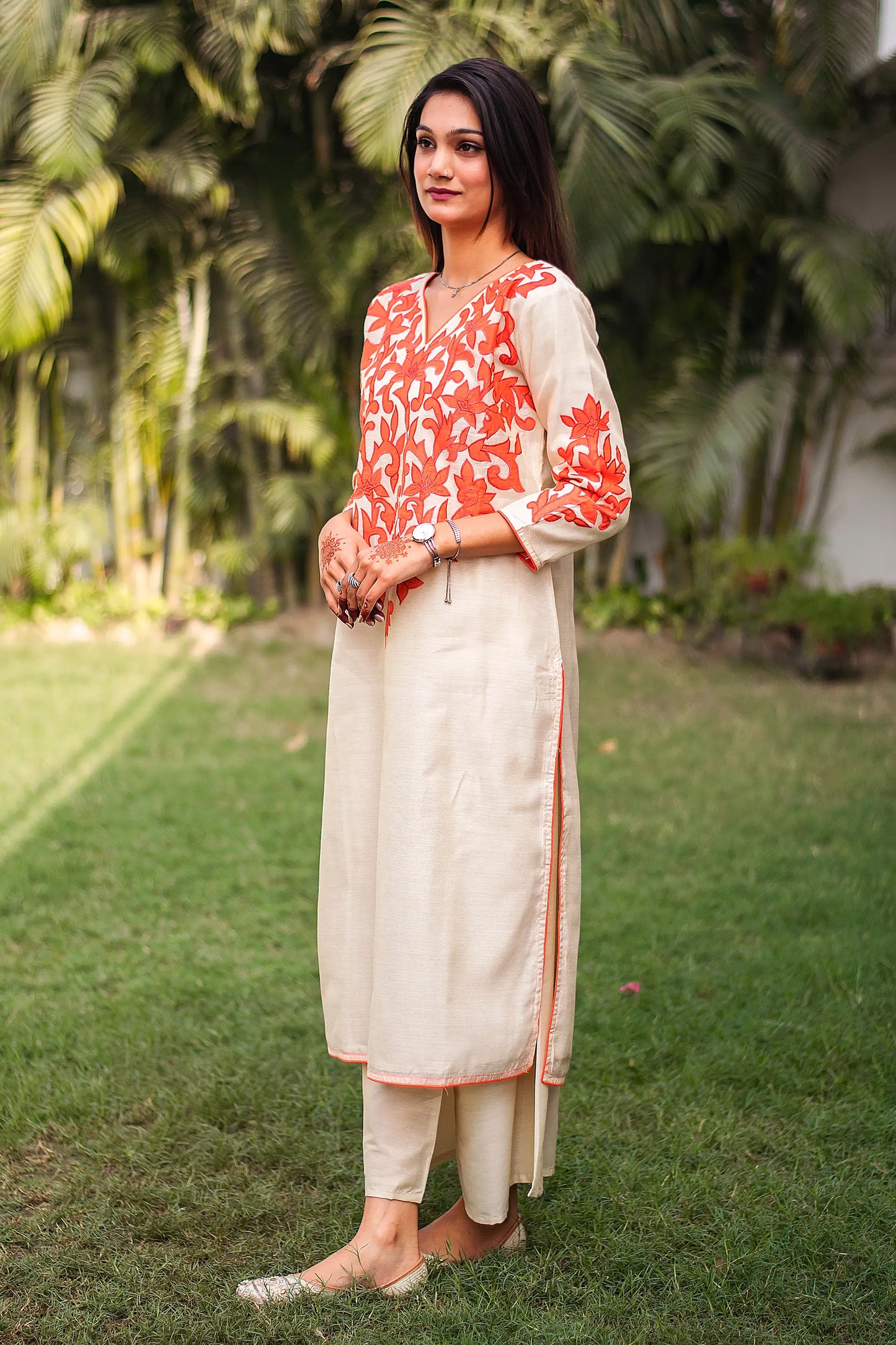 Side view of an Indian model in a beige chanderi kurta with orange floral patchwork, complemented by beige palazzo.